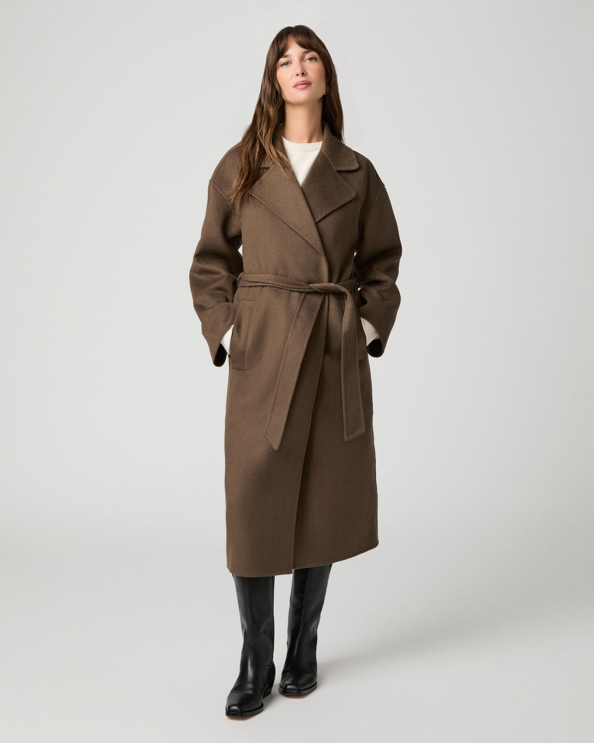 Woman wearing long brown coat and black boots against a white background