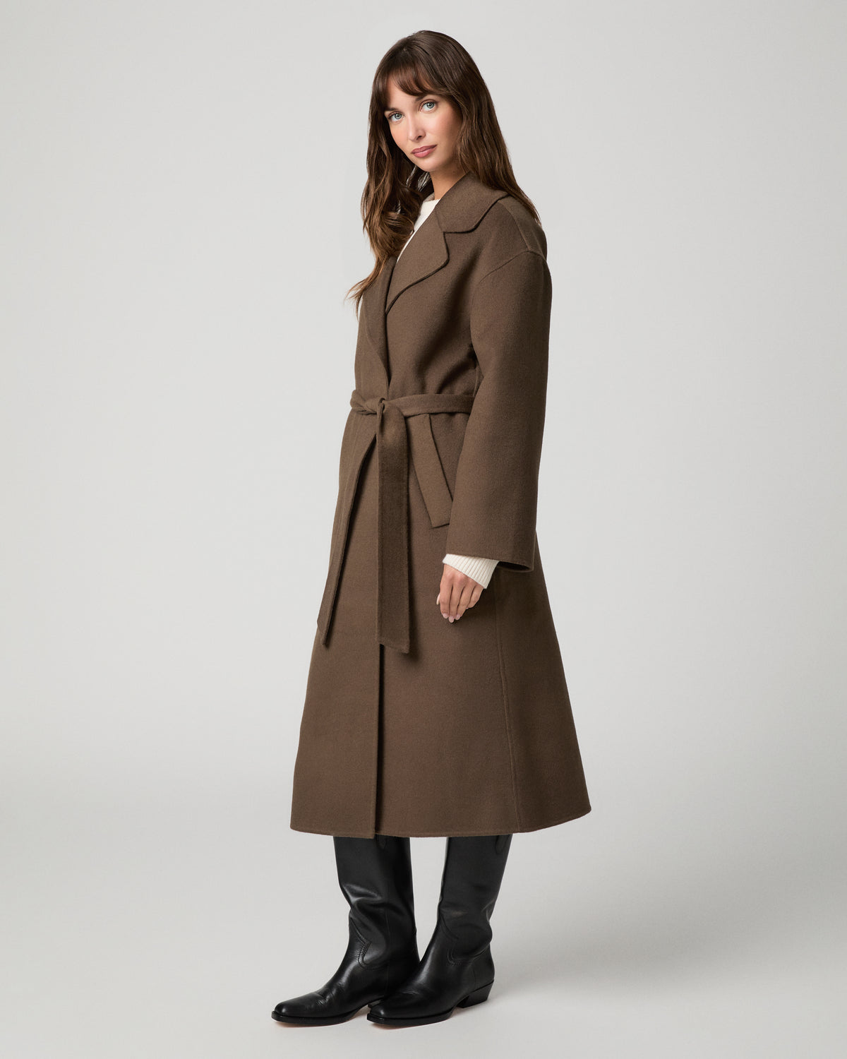 Woman wearing long brown coat and black boots against a white background