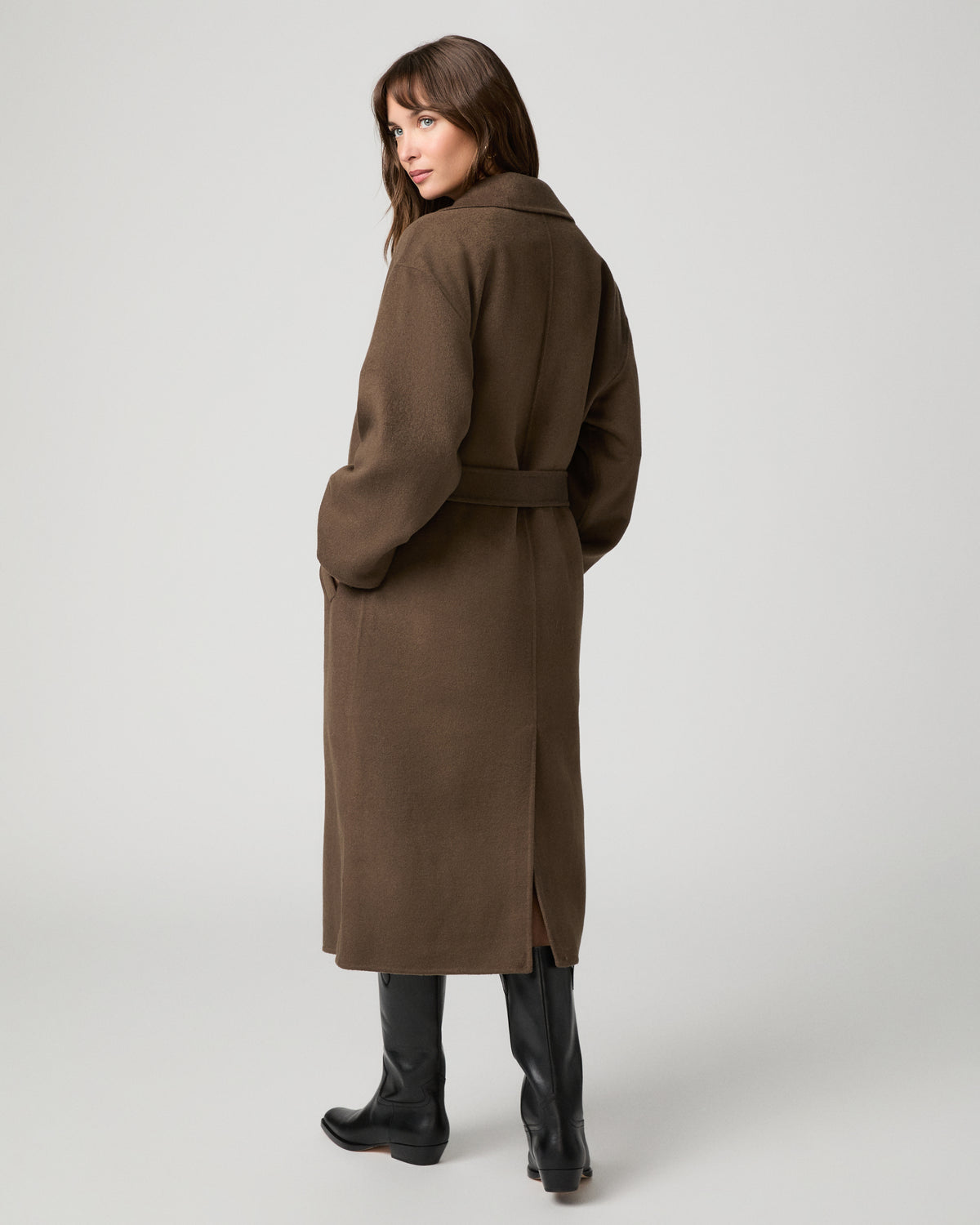 Woman wearing long brown coat and black boots against a white background