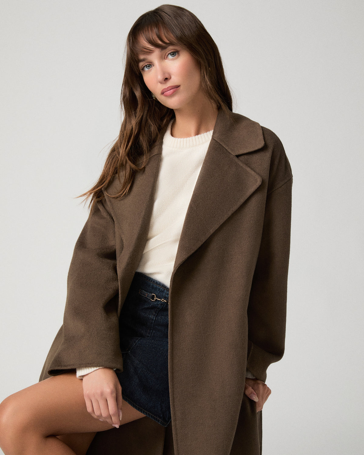 Woman wearing long brown coat and black boots against a white background