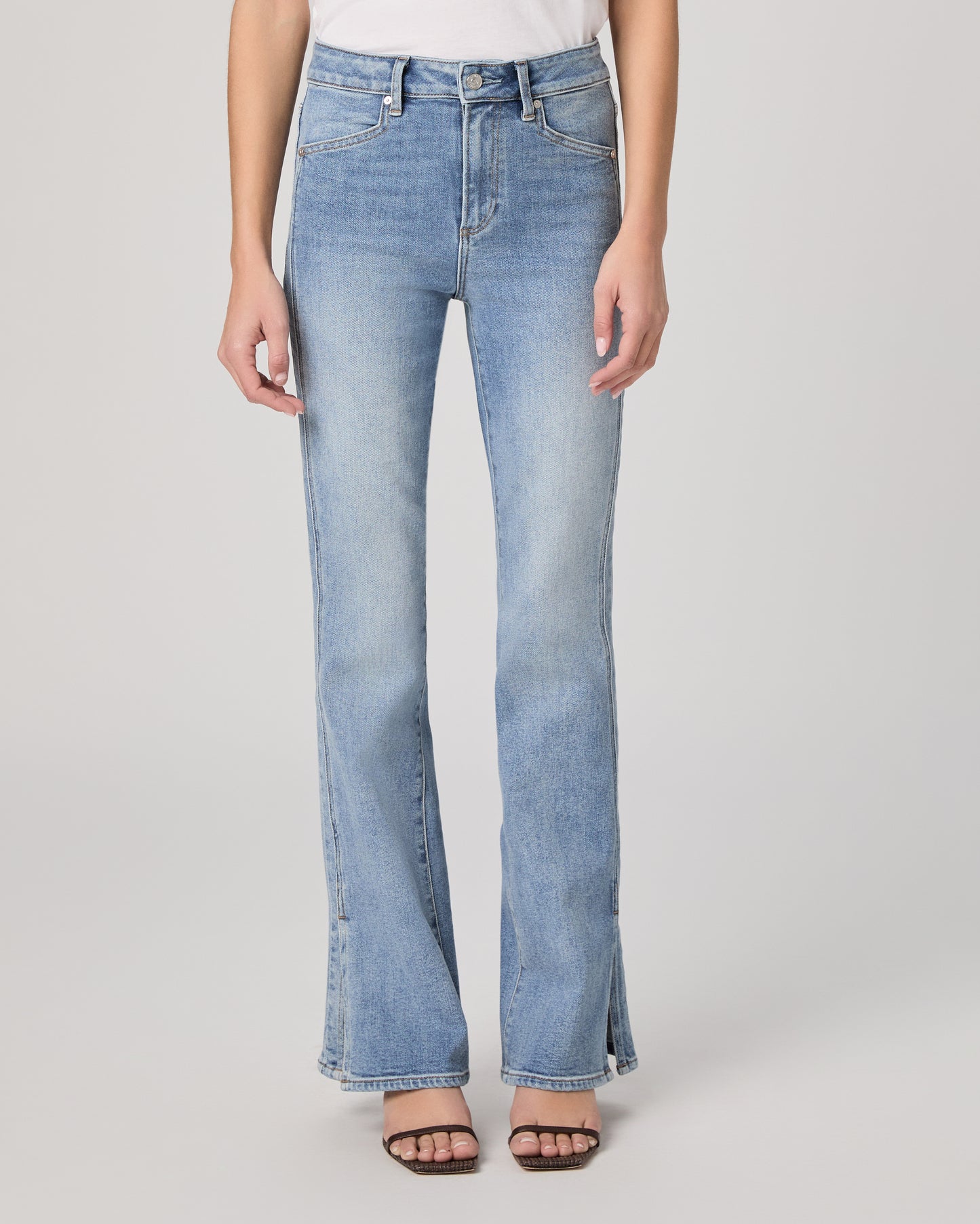 Woman wearing a white blouse and blue jeans paired with brown heels on a plain background