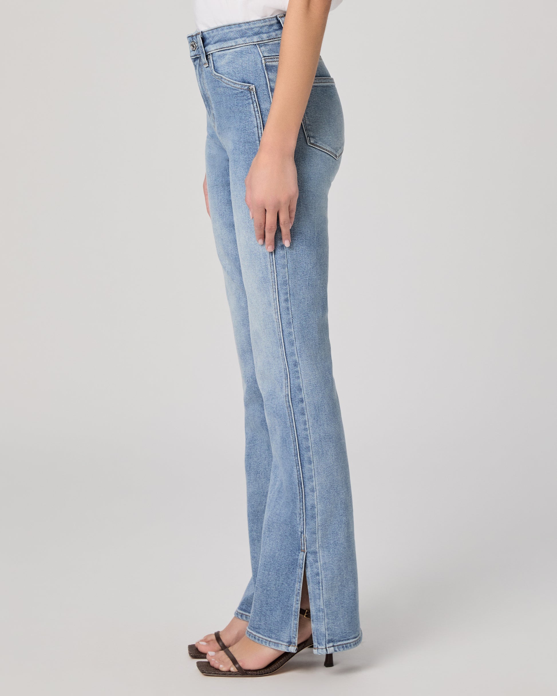 Woman wearing a white blouse and blue jeans paired with brown heels on a plain background