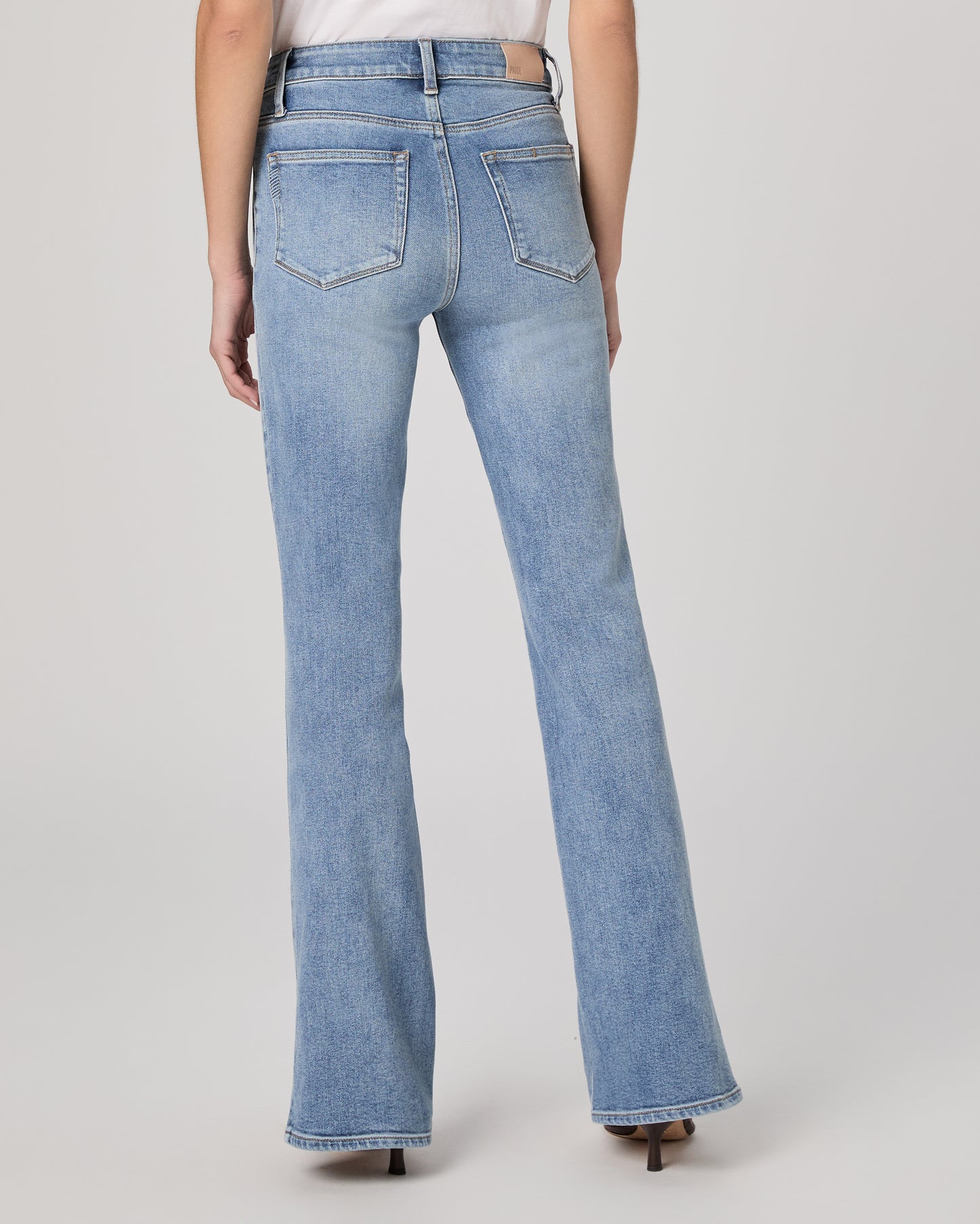 Woman wearing a white blouse and blue jeans paired with brown heels on a plain background