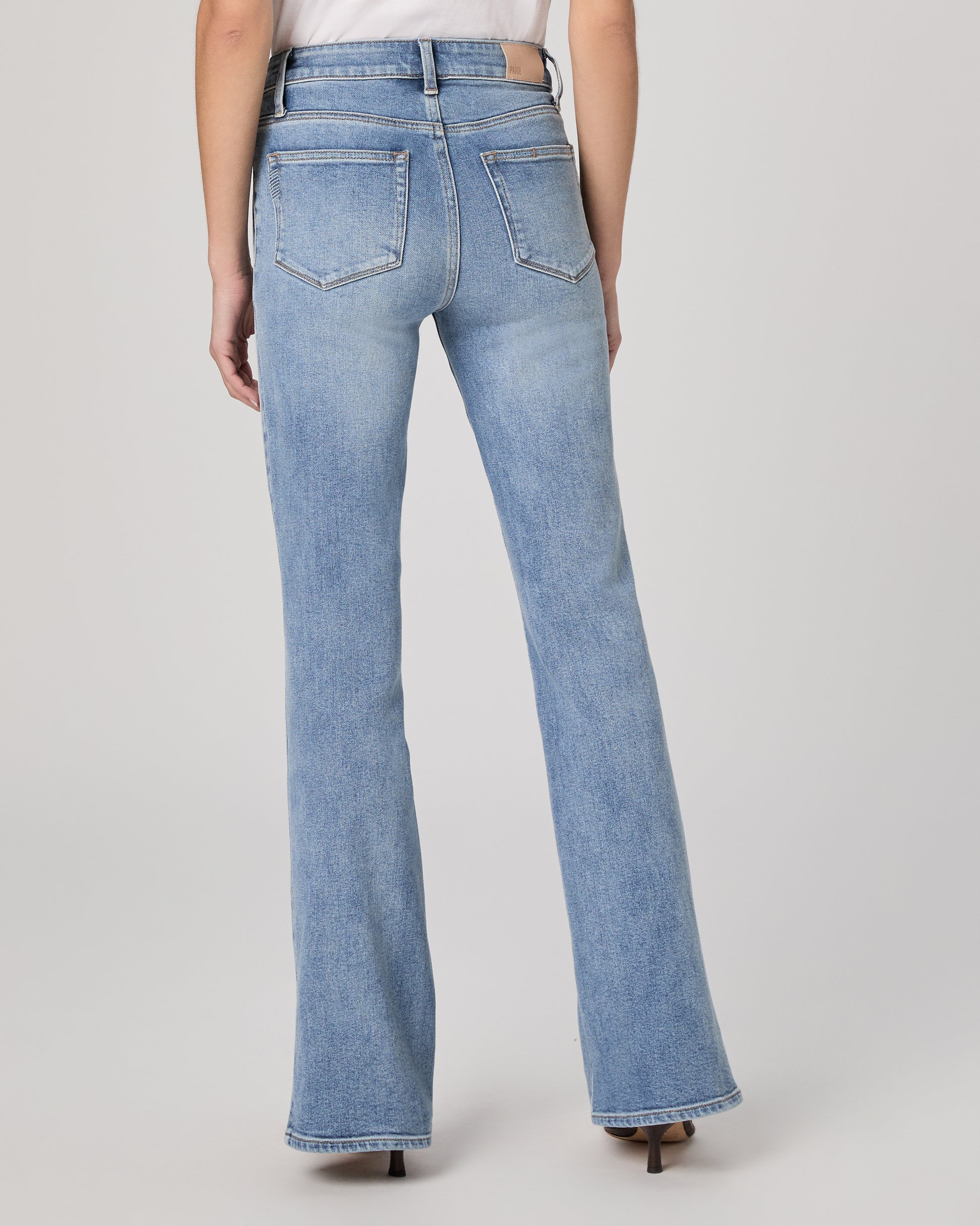 Woman wearing a white blouse and blue jeans paired with brown heels on a plain background