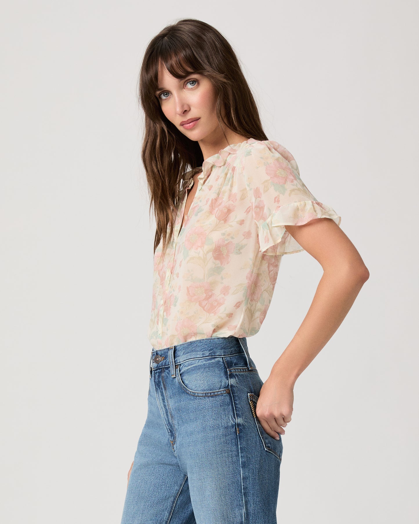 Woman wearing a flower printed light pink blouse and blue jeans on a white plain background