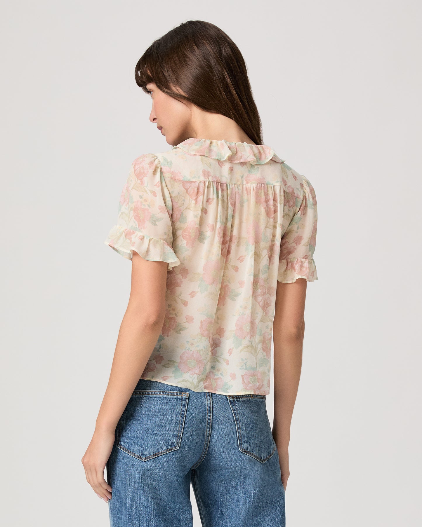 Woman wearing a flower printed light pink blouse and blue jeans on a white plain background