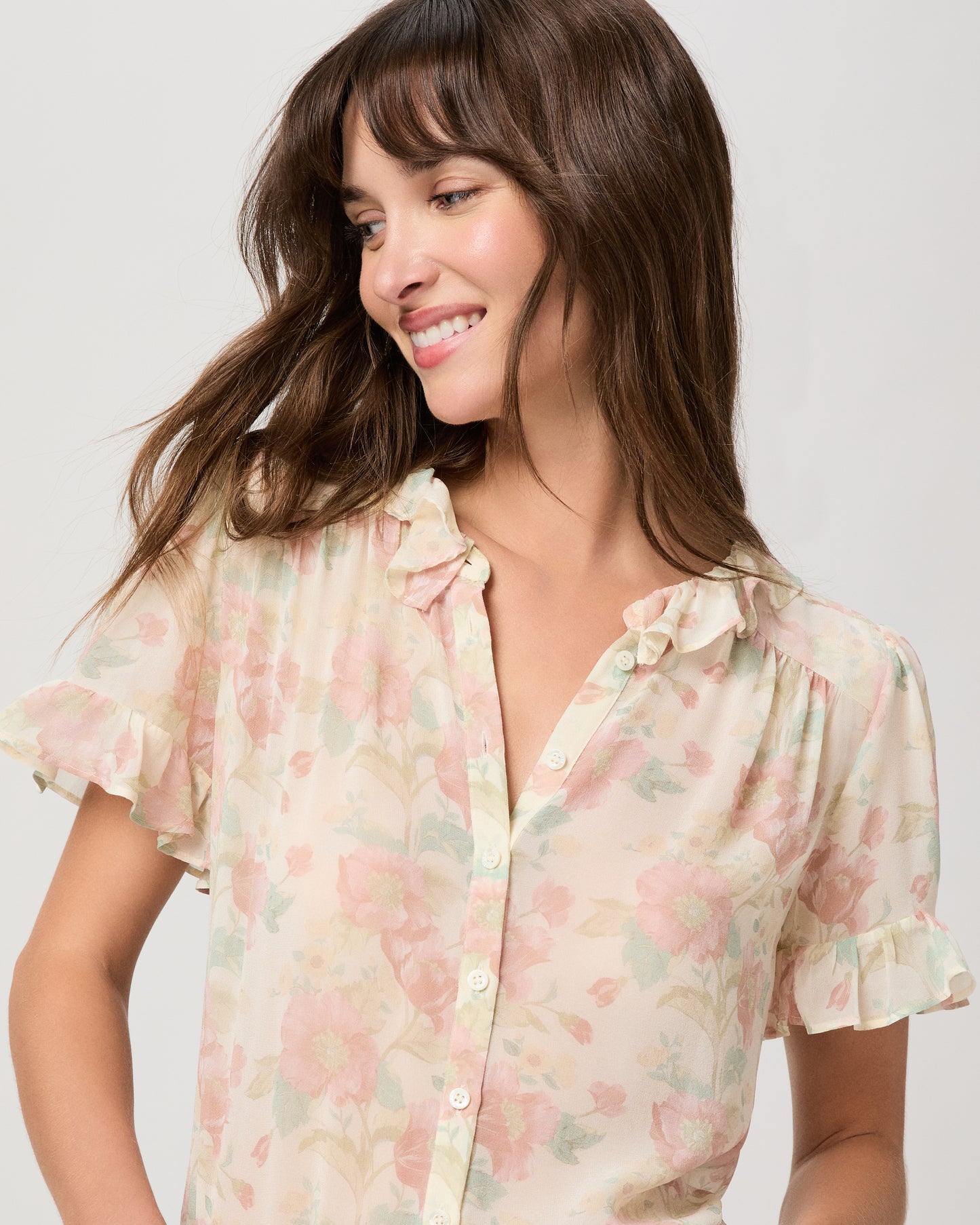 Woman wearing a flower printed light pink blouse and blue jeans on a white plain background