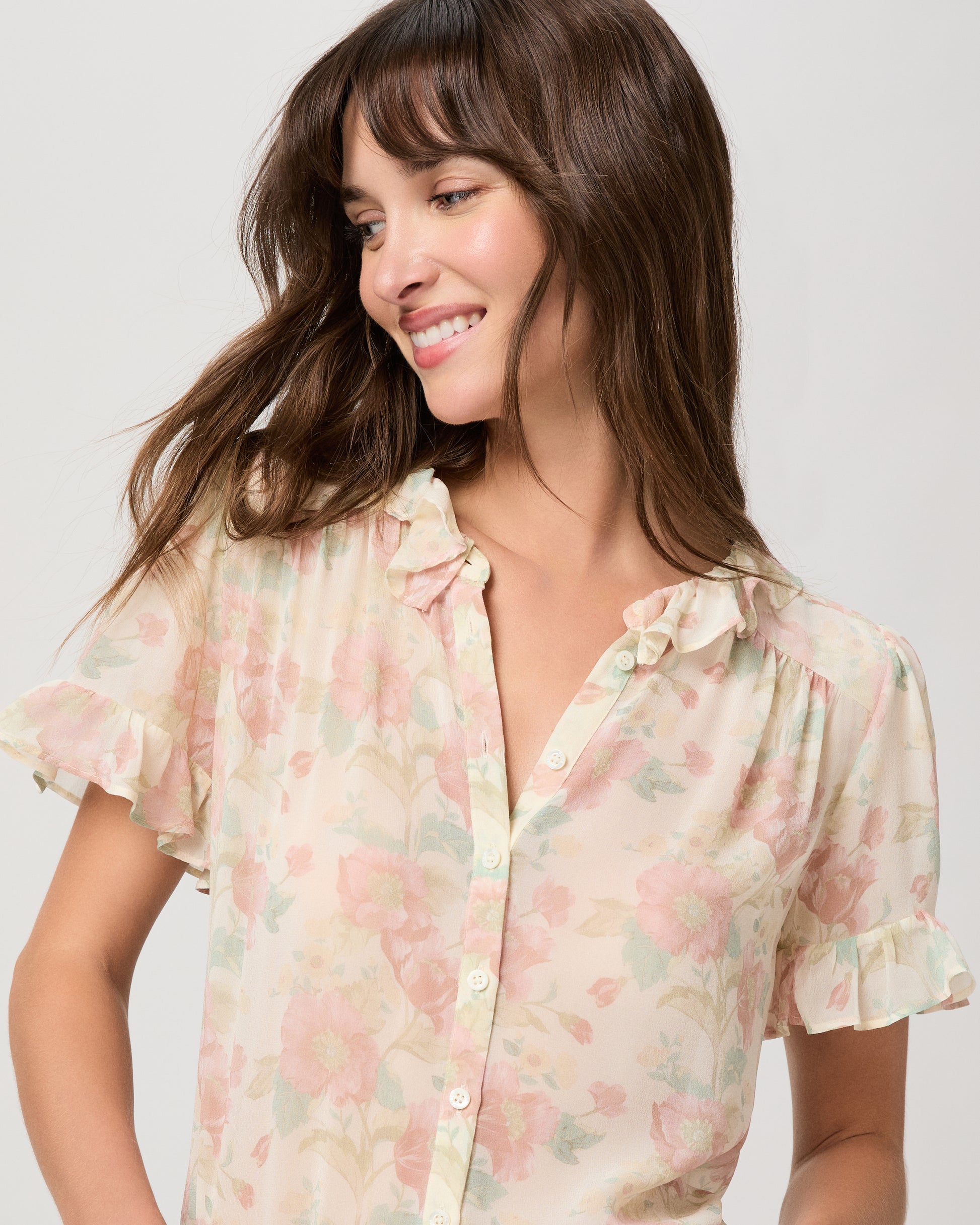 Woman wearing a flower printed light pink blouse and blue jeans on a white plain background