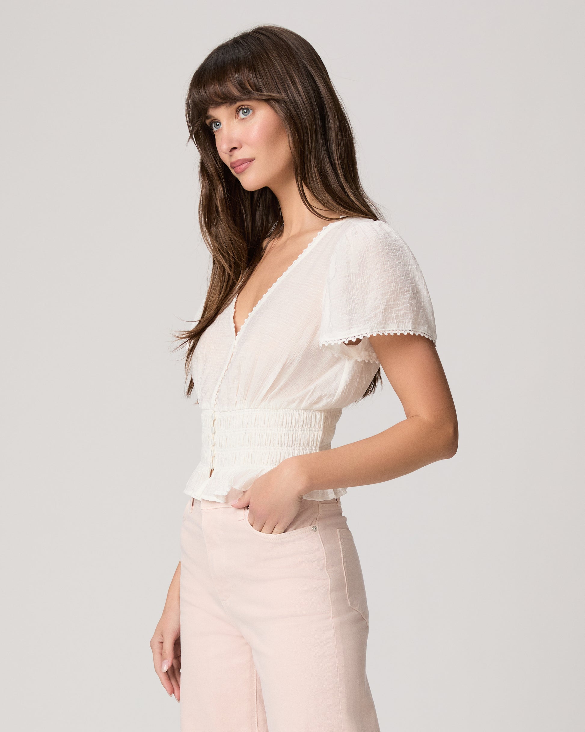 Woman wearing a white blouse and light pink pants against a plain background