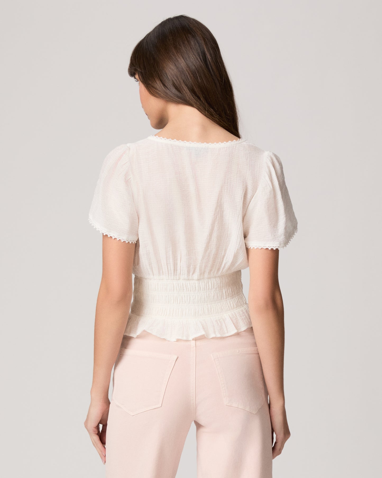 Woman wearing a white blouse and light pink pants against a plain background