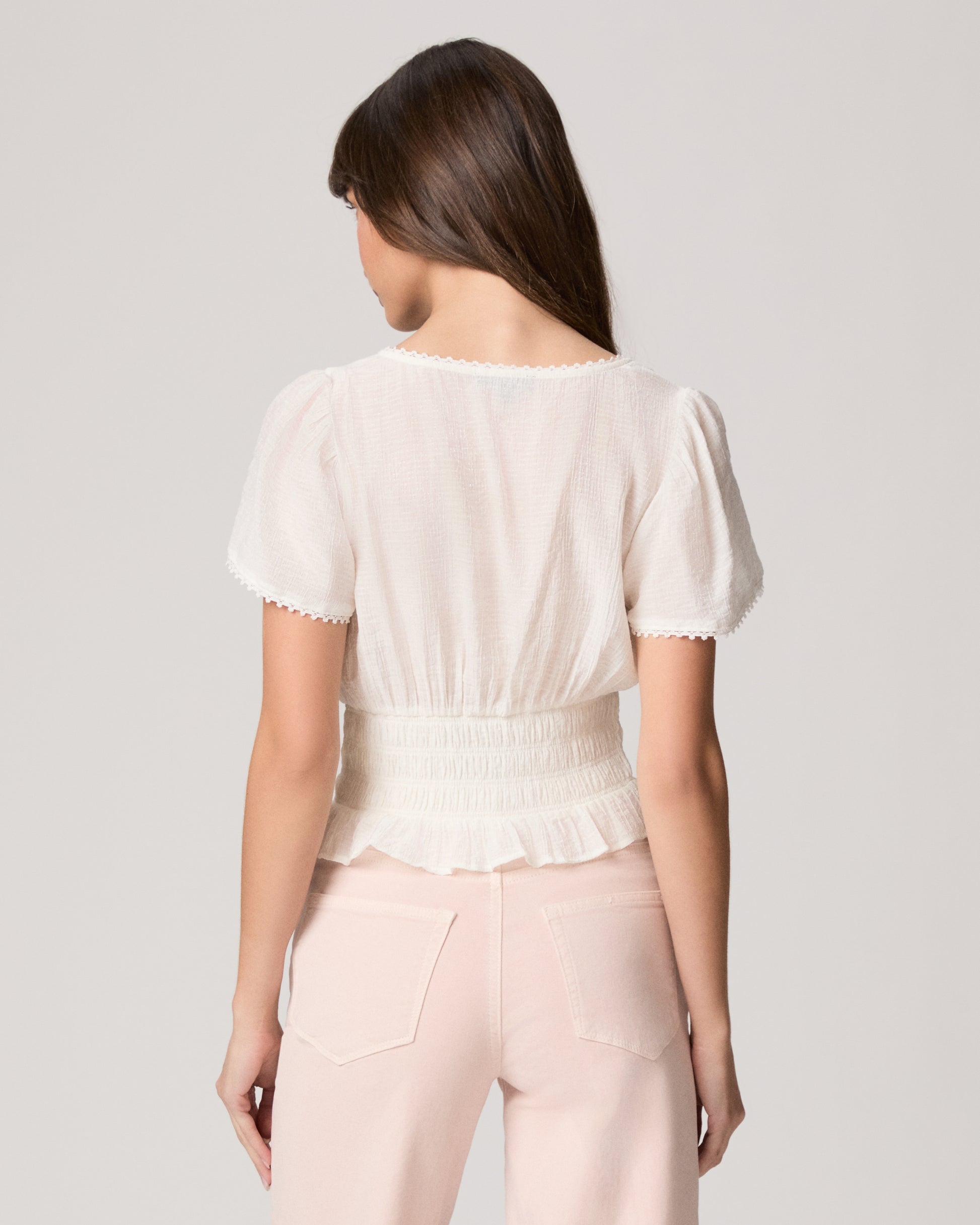 Woman wearing a white blouse and light pink pants against a plain background