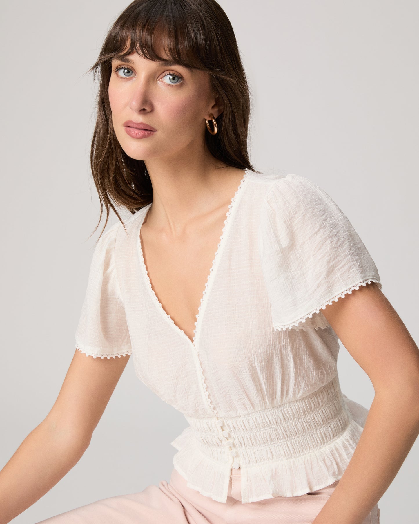 Woman wearing a white blouse and light pink pants against a plain background