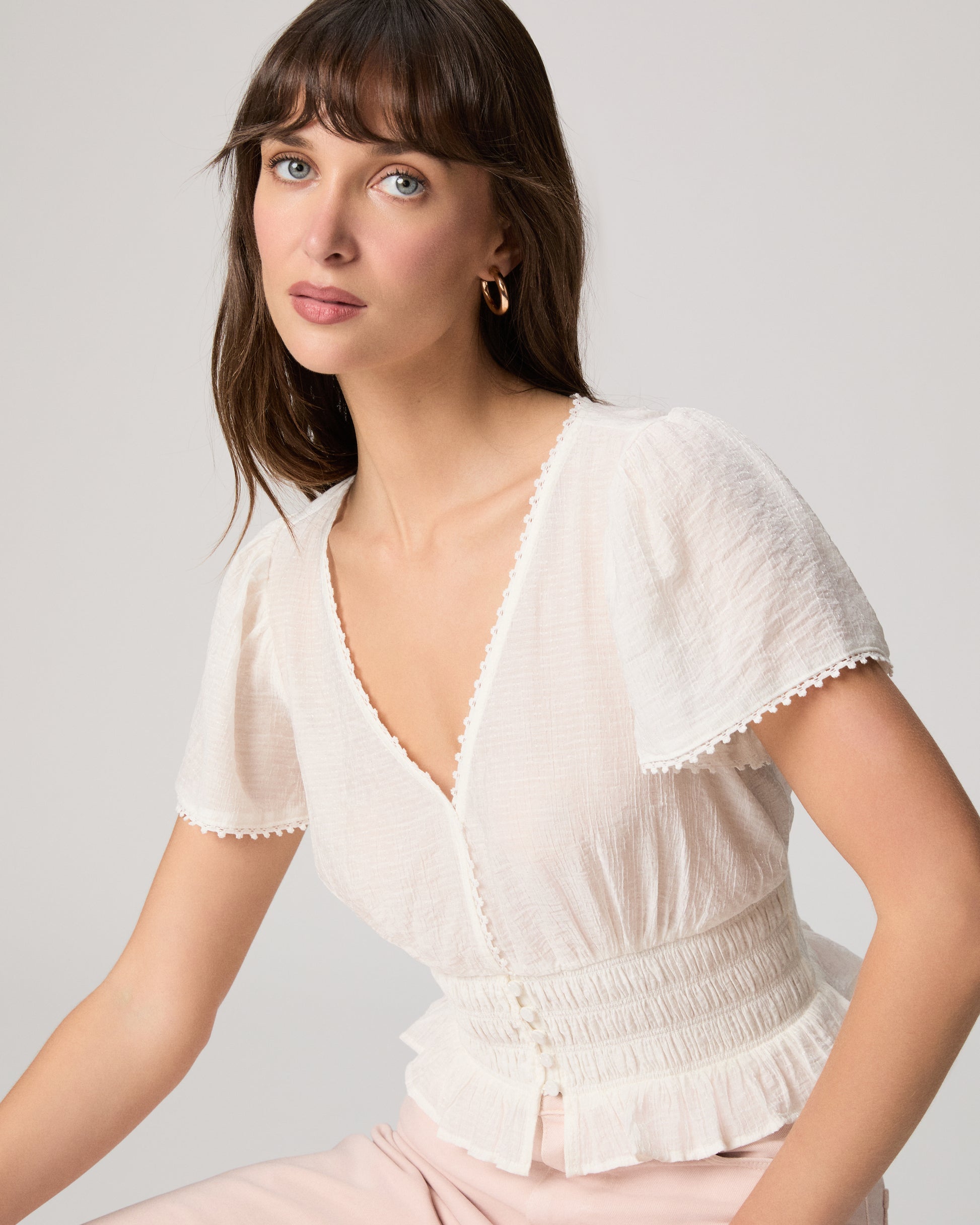 Woman wearing a white blouse and light pink pants against a plain background