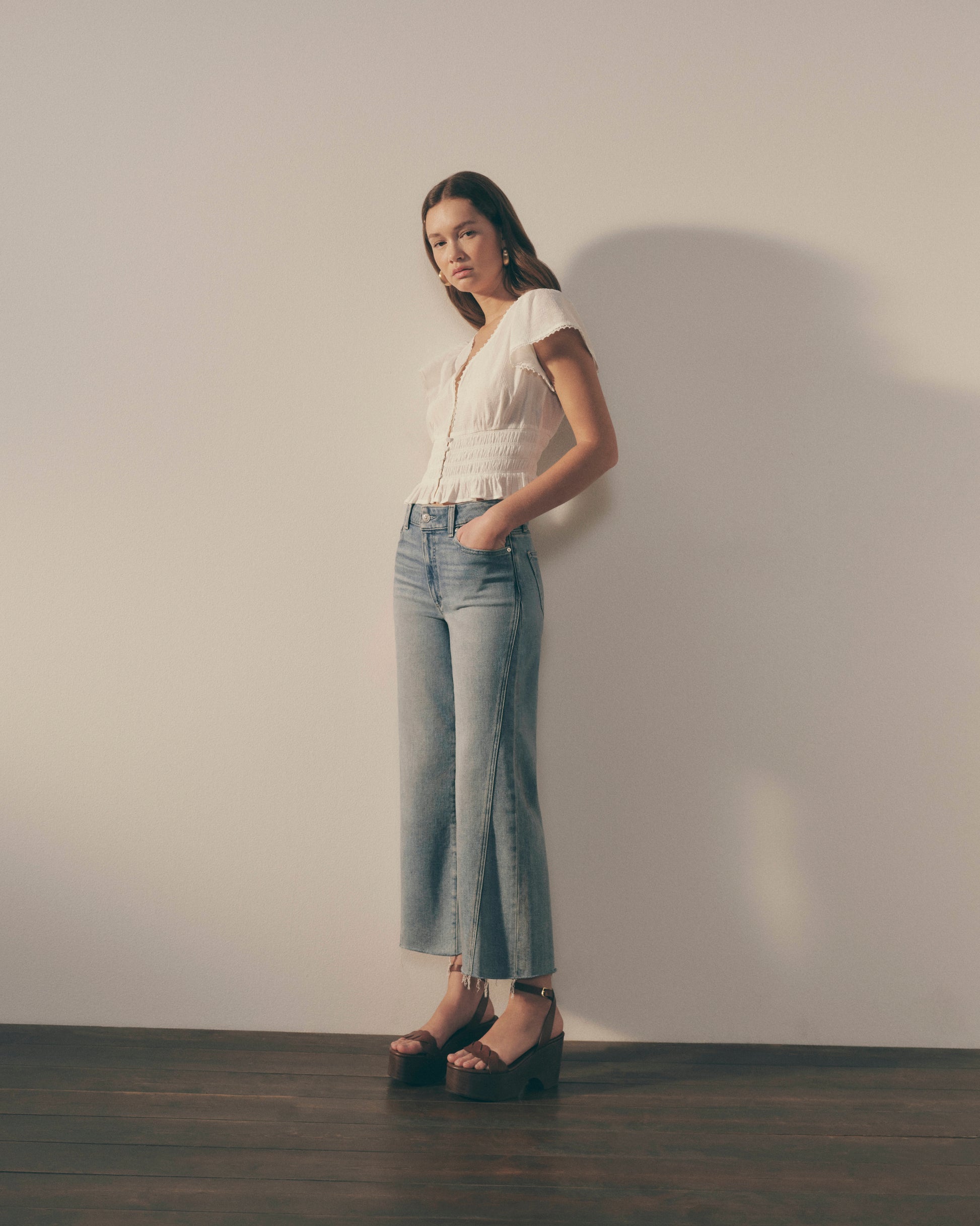 Woman wearing a white blouse and blue jeans standing against a plain background