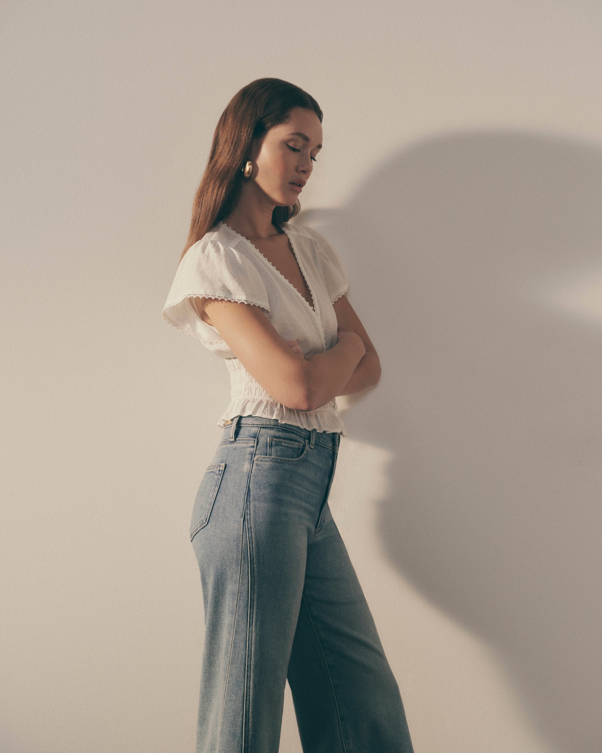 Woman wearing a white blouse and light blue jeans against a plain background