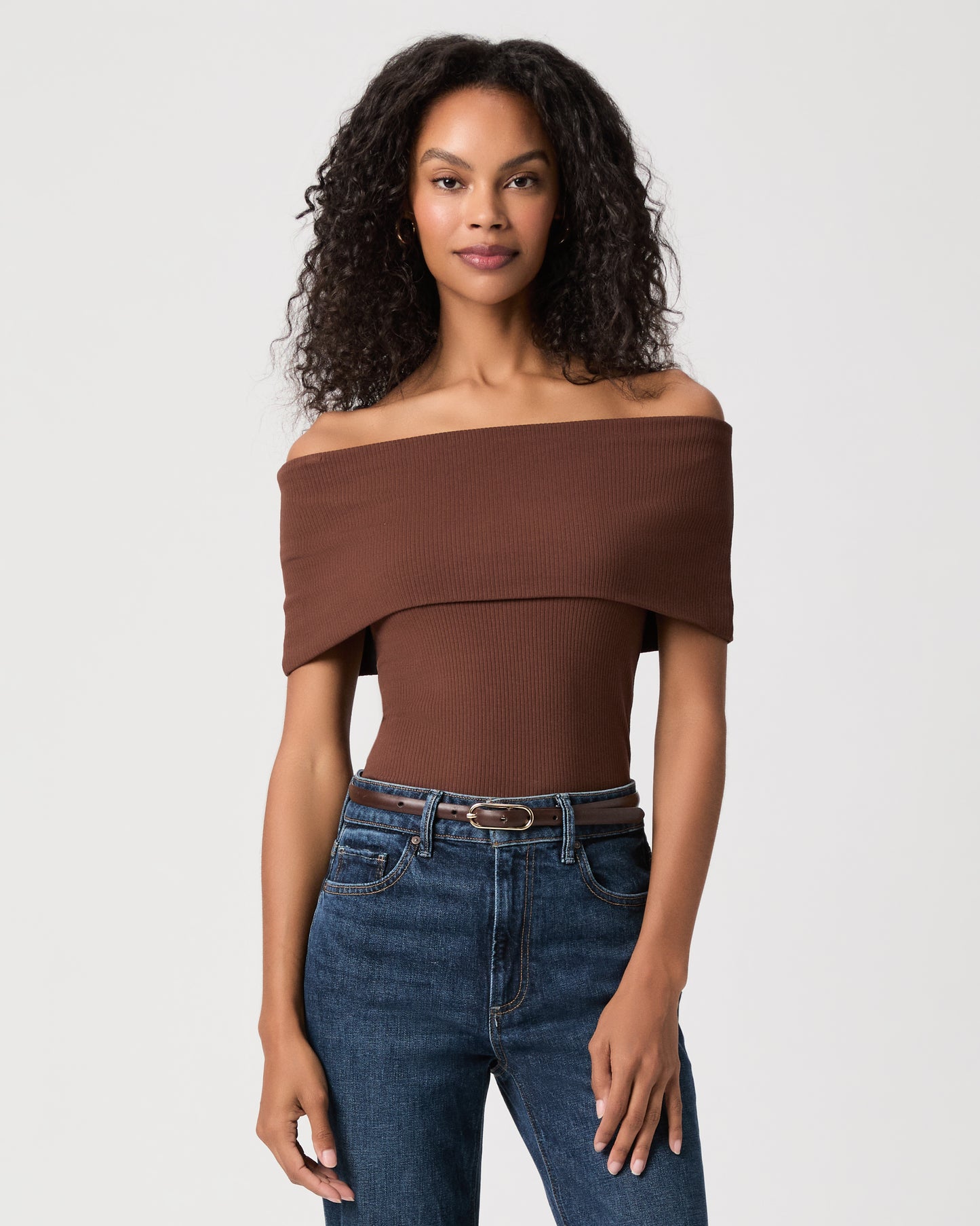 women wearing a brown off the shoulder top and blue jeans against a white background 
