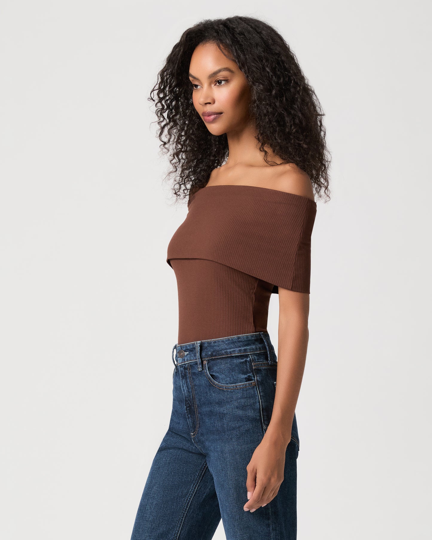 women wearing a brown off the shoulder top and blue jeans against a white background 