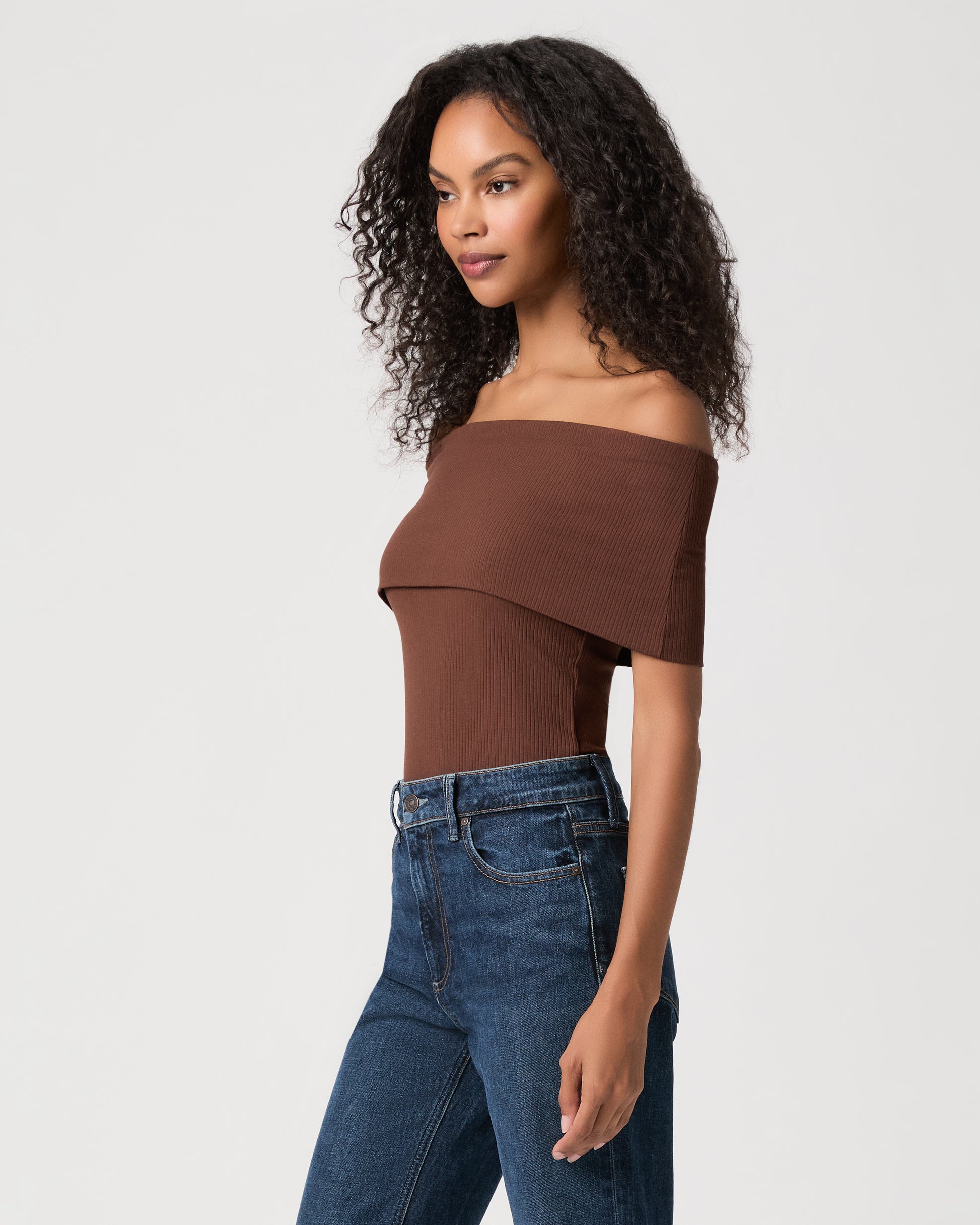 women wearing a brown off the shoulder top and blue jeans against a white background 