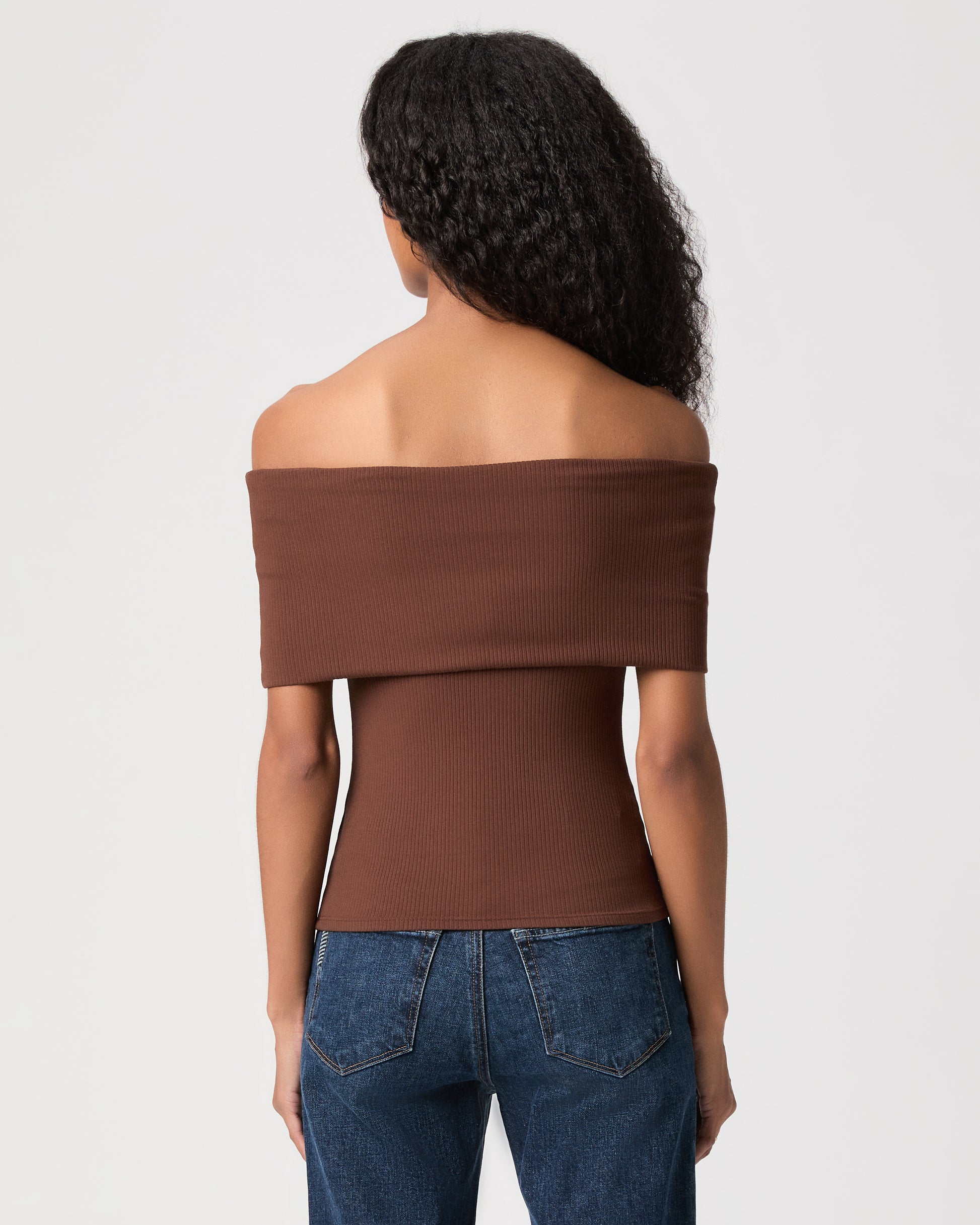 women wearing a brown off the shoulder top and blue jeans against a white background 