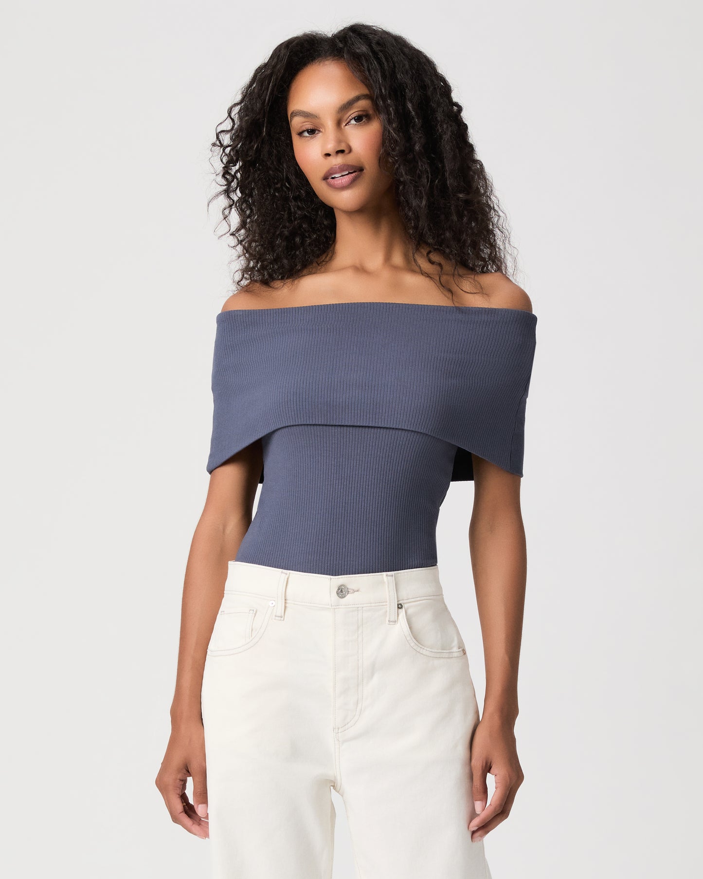 women wearing a blue off the shoulder top paired with white jeans against a white background 