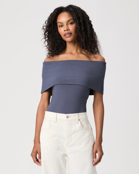 women wearing a blue off the shoulder top paired with white jeans against a white background 