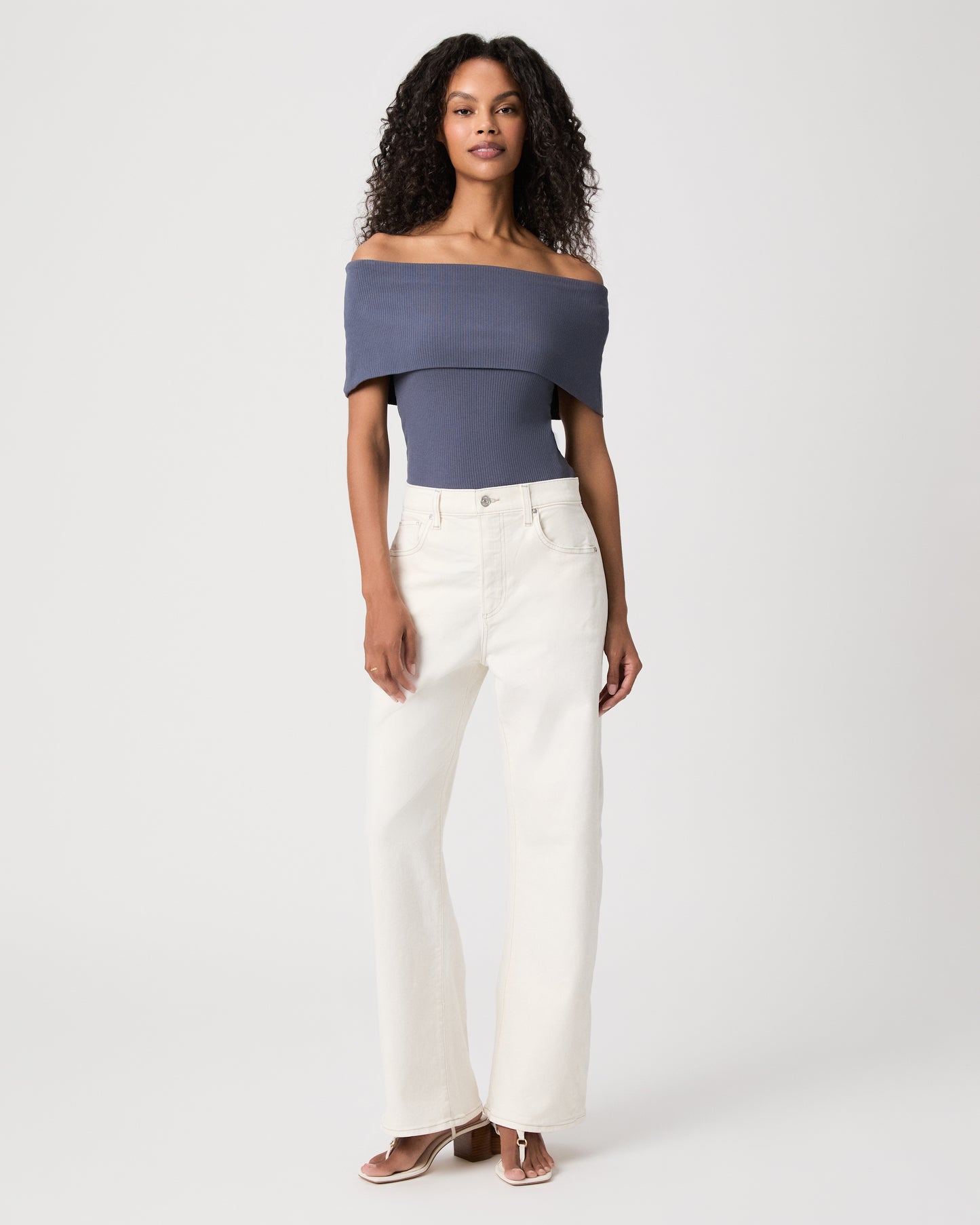 women wearing a blue off the shoulder top paired with white jeans against a white background 
