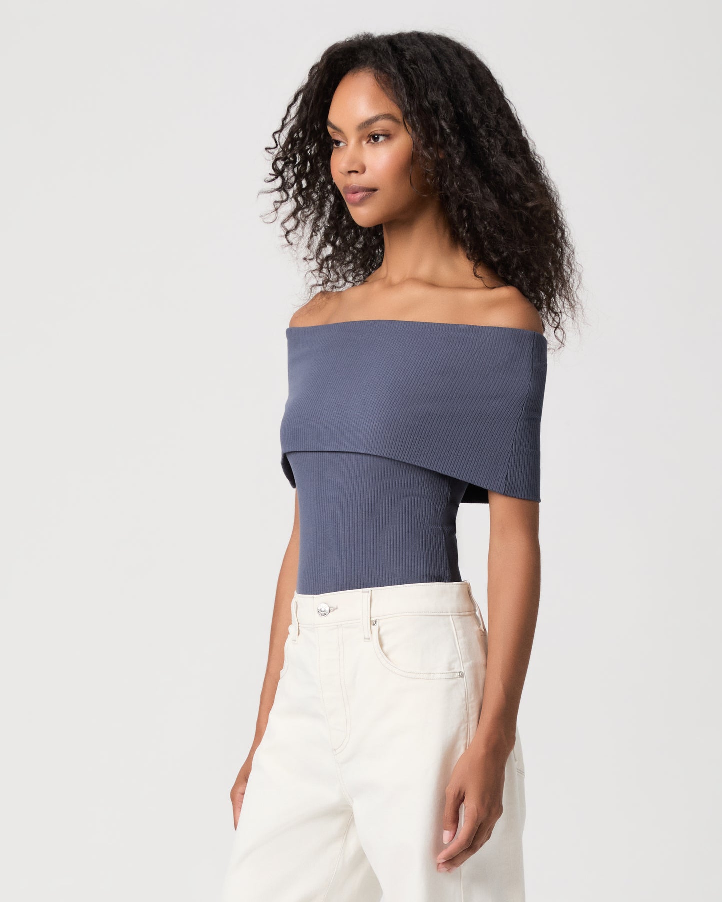 women wearing a blue off the shoulder top paired with white jeans against a white background 