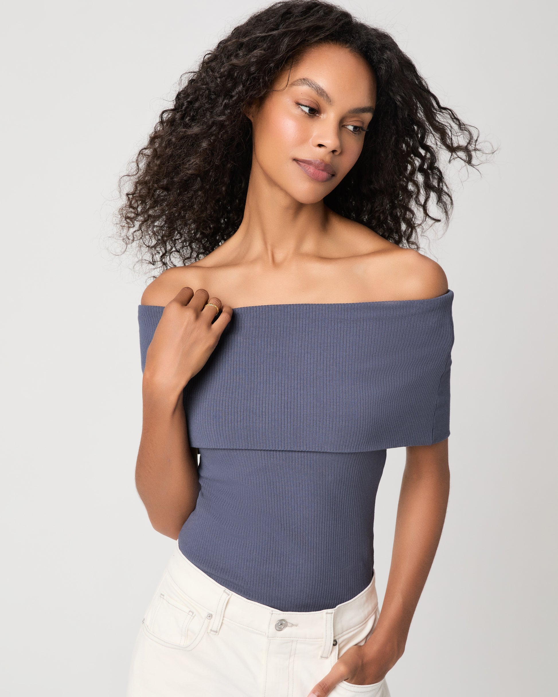 women wearing a blue off the shoulder top paired with white jeans against a white background 