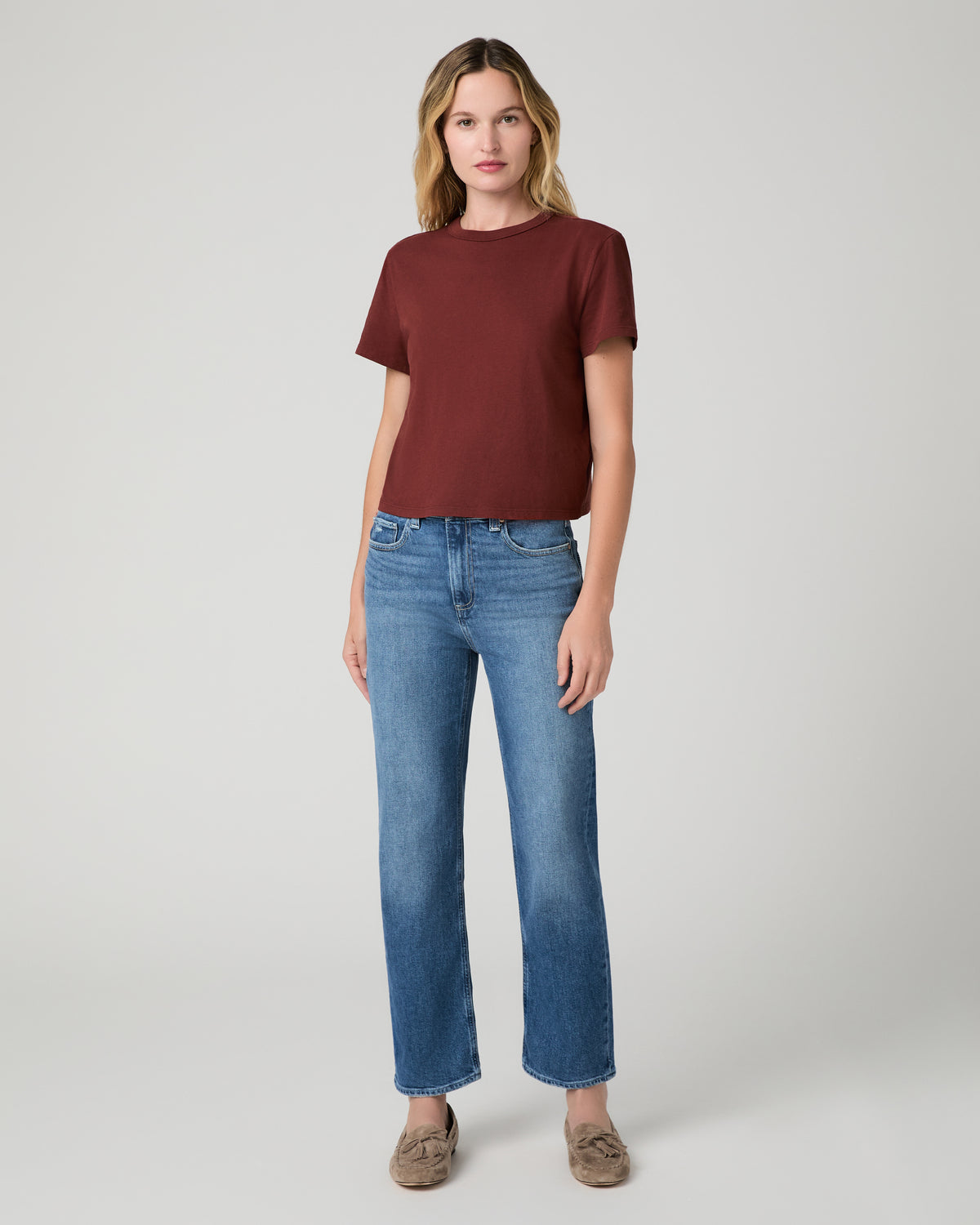 Women wearing red tee and blue jeans paired with brown flats against a white background