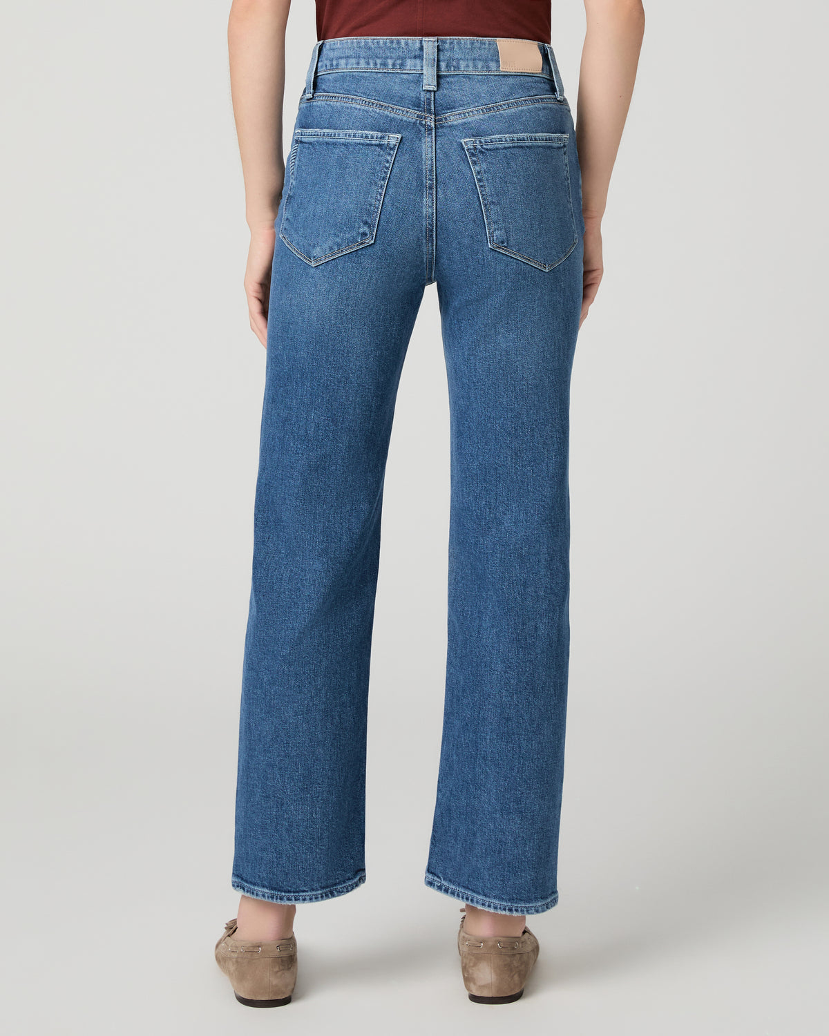 Women wearing red tee and blue jeans paired with brown flats against a white background