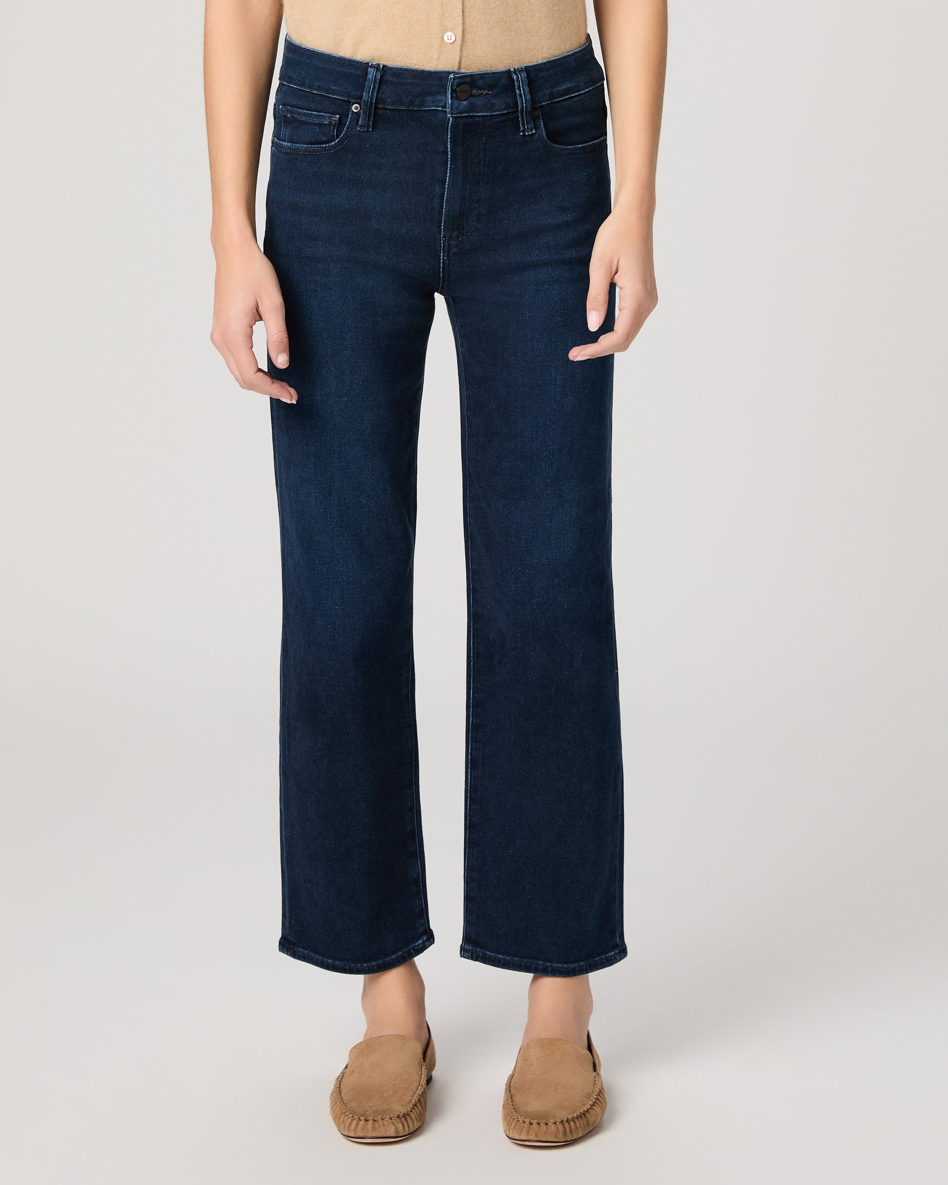 Woman wearing a beige sleeveless top and dark blue jeans on a white background