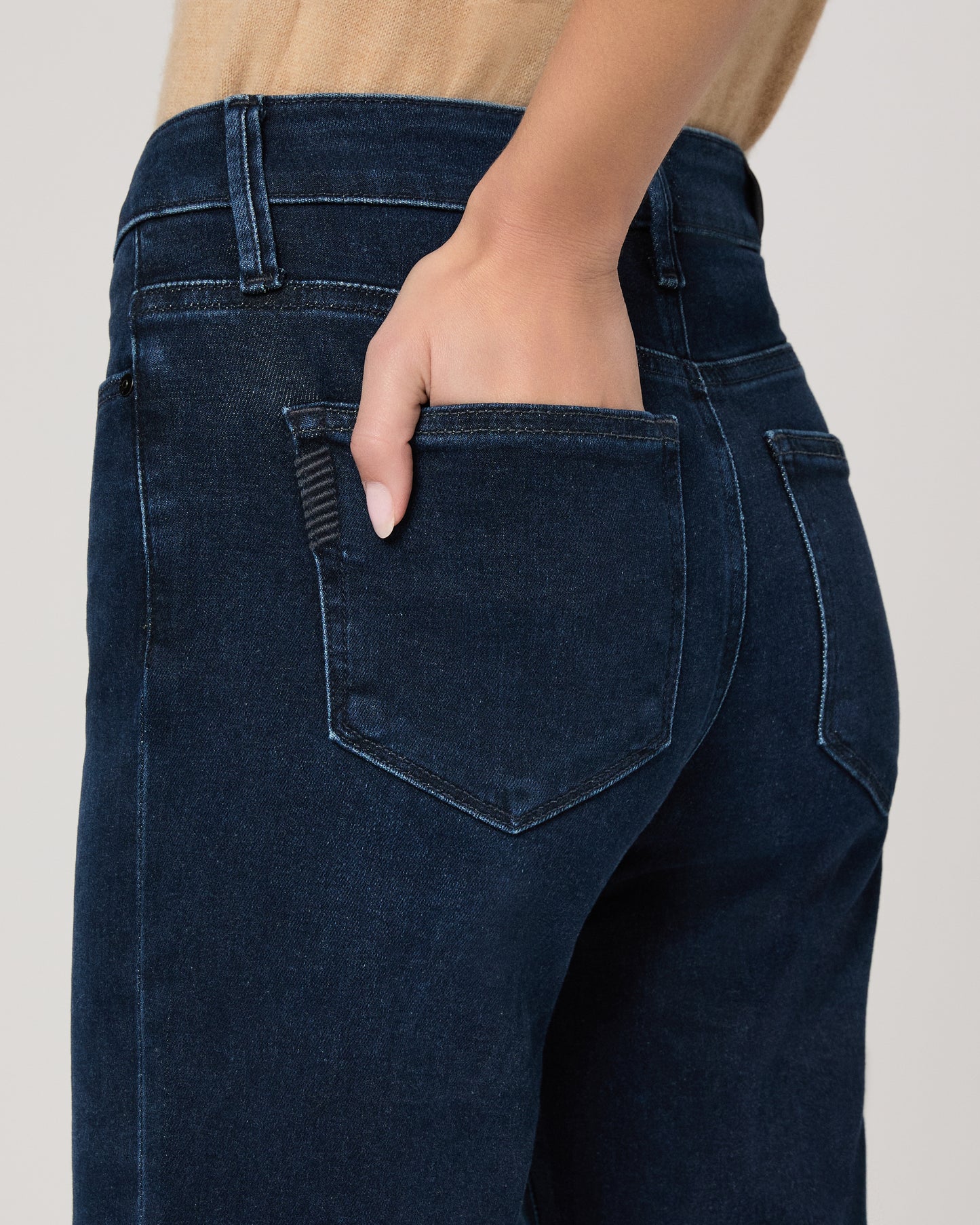 Woman wearing a beige sleeveless top and dark blue jeans on a white background