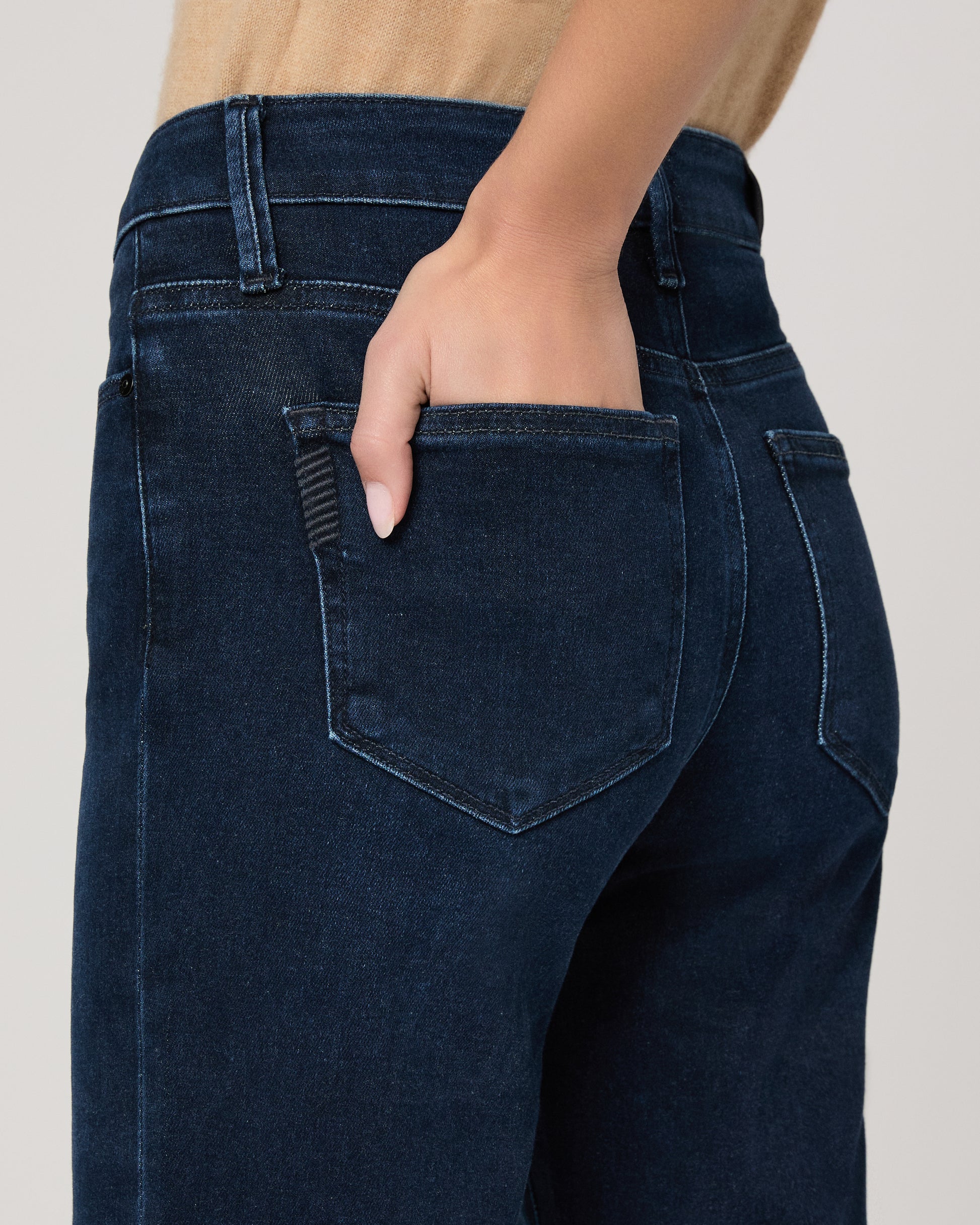 Woman wearing a beige sleeveless top and dark blue jeans on a white background