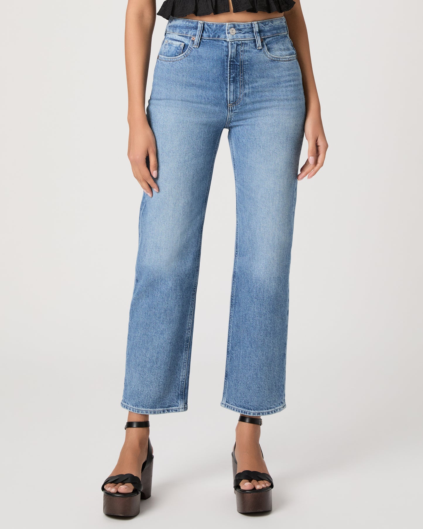 Woman wearing a black top and blue jeans paired with black heels on a white background