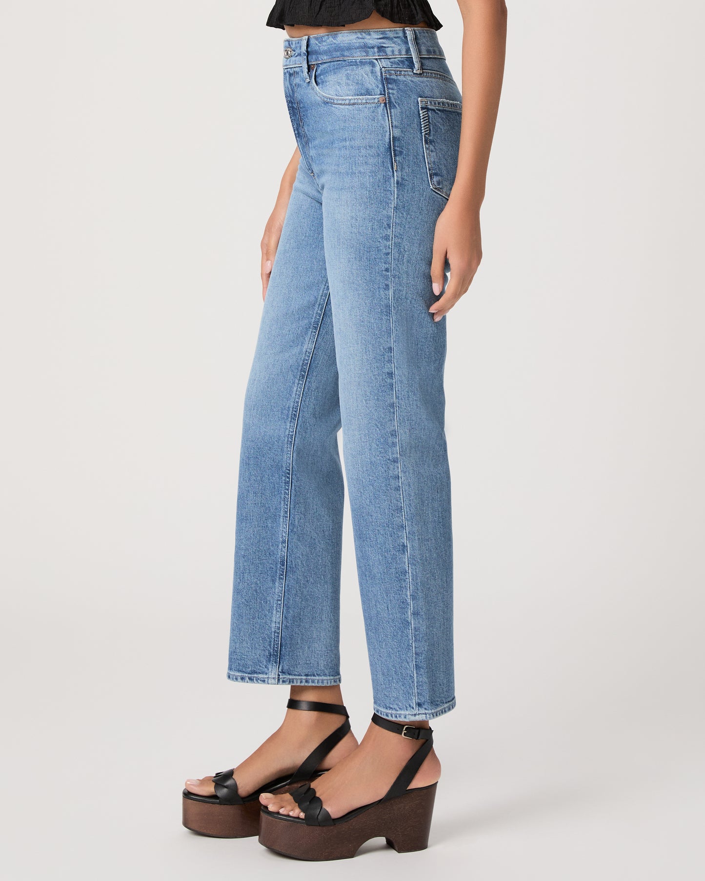 Woman wearing a black top and blue jeans paired with black heels on a white background