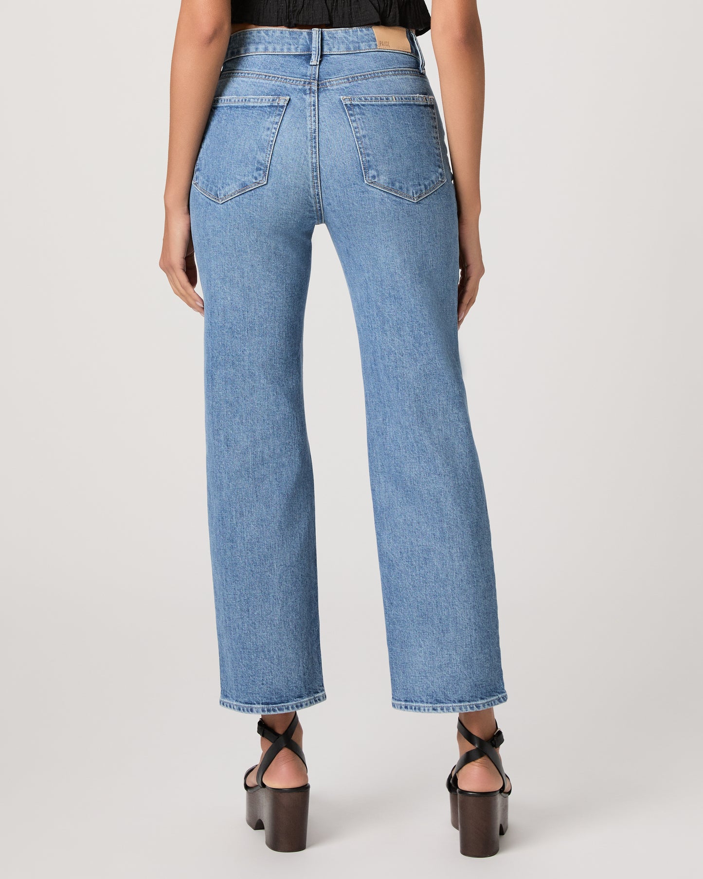 Woman wearing a black top and blue jeans paired with black heels on a white background