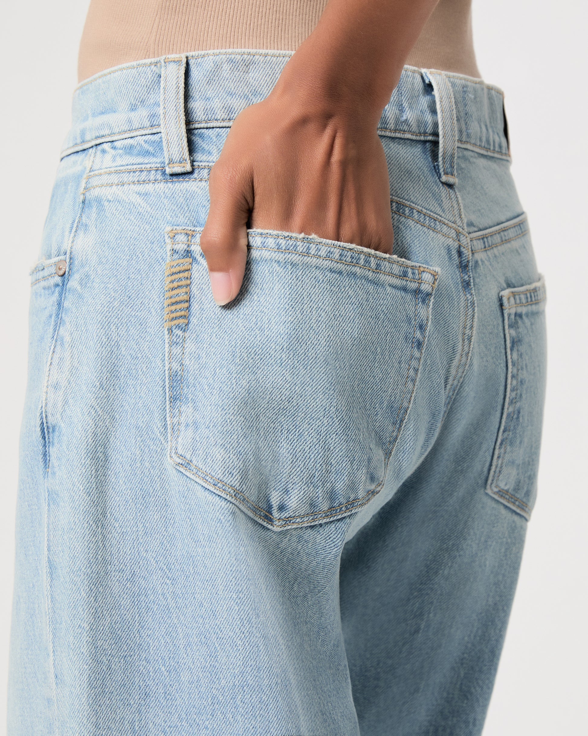 Close-up of a person wearing light-wash blue denim jeans, with a hand reaching into the back pocket.