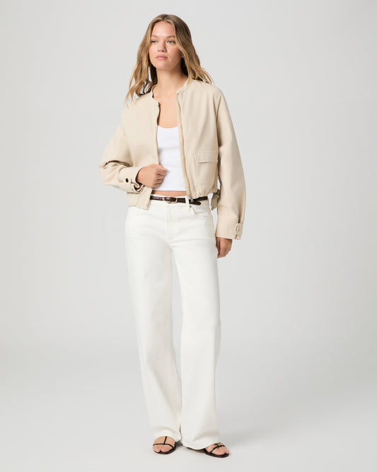 Women wearing a beige jacket, white tank paired with white jeans and a black belt with black sandals 