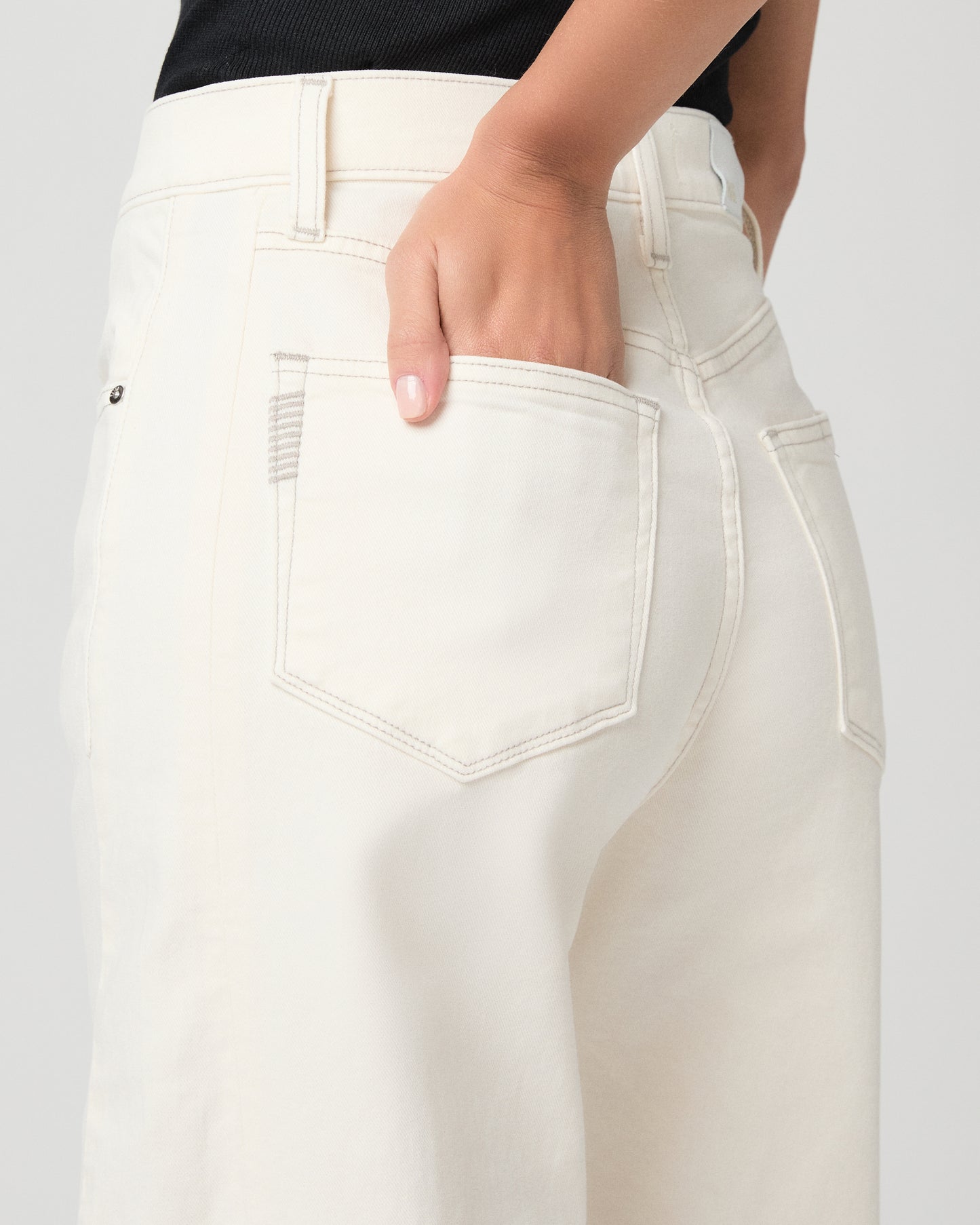 Woman wearing a black tank top and white pants and snake print sandals on a plain background