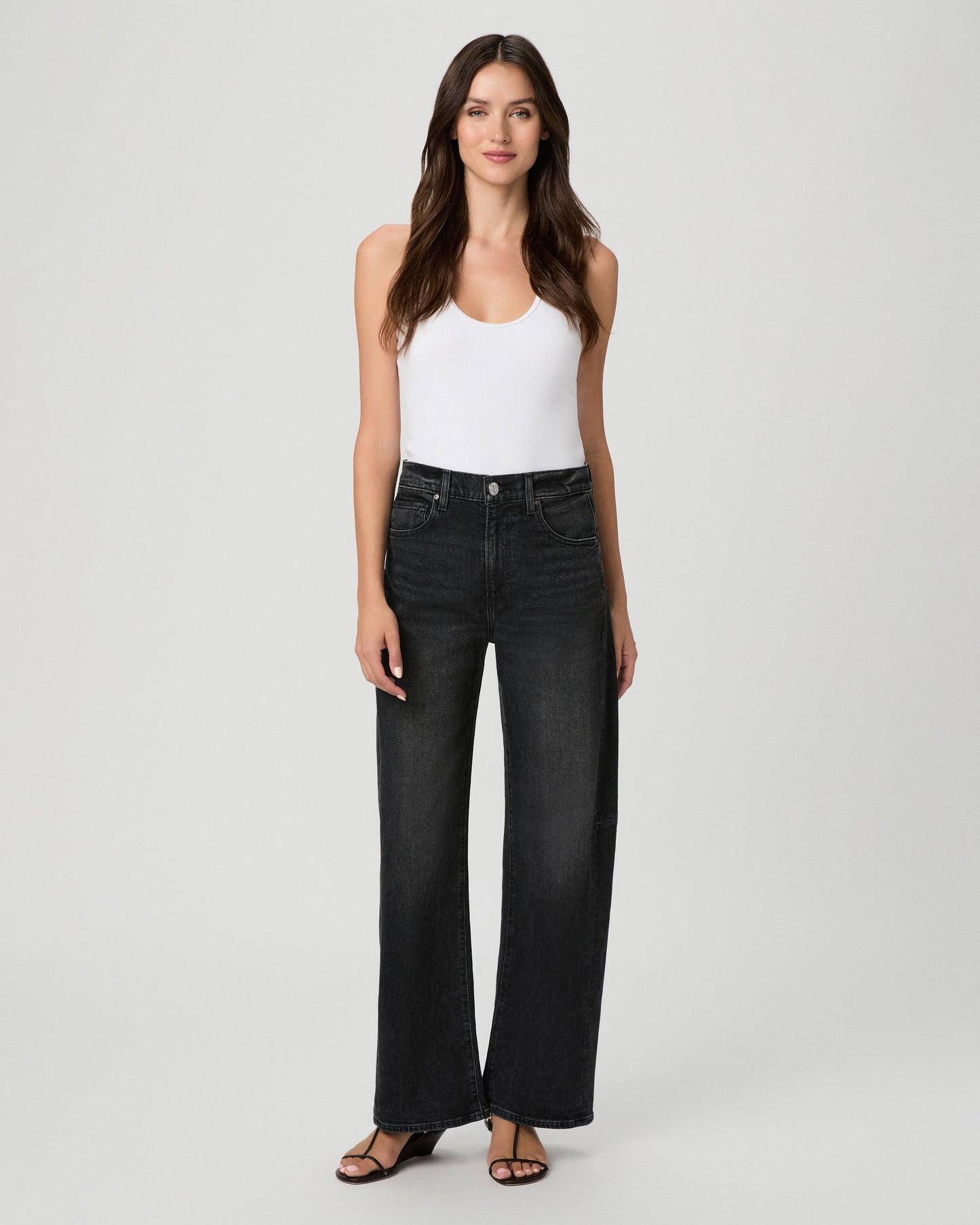 Woman wearing a white top paired with black  jeans and black sandals against a white background