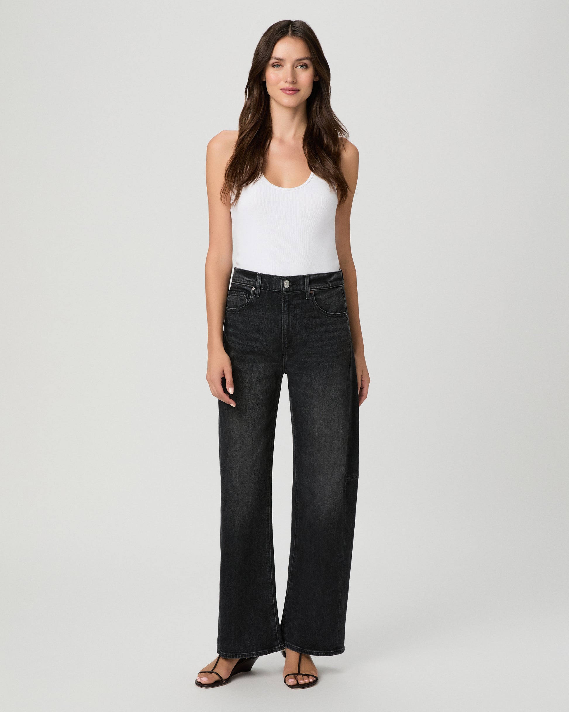 Woman wearing a white top paired with black  jeans and black sandals against a white background