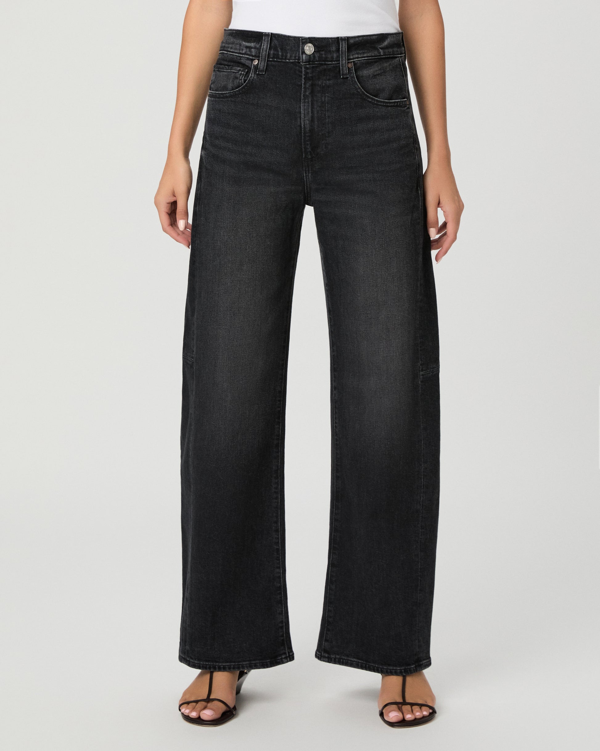 Woman wearing a white top paired with black  jeans and black sandals against a white background