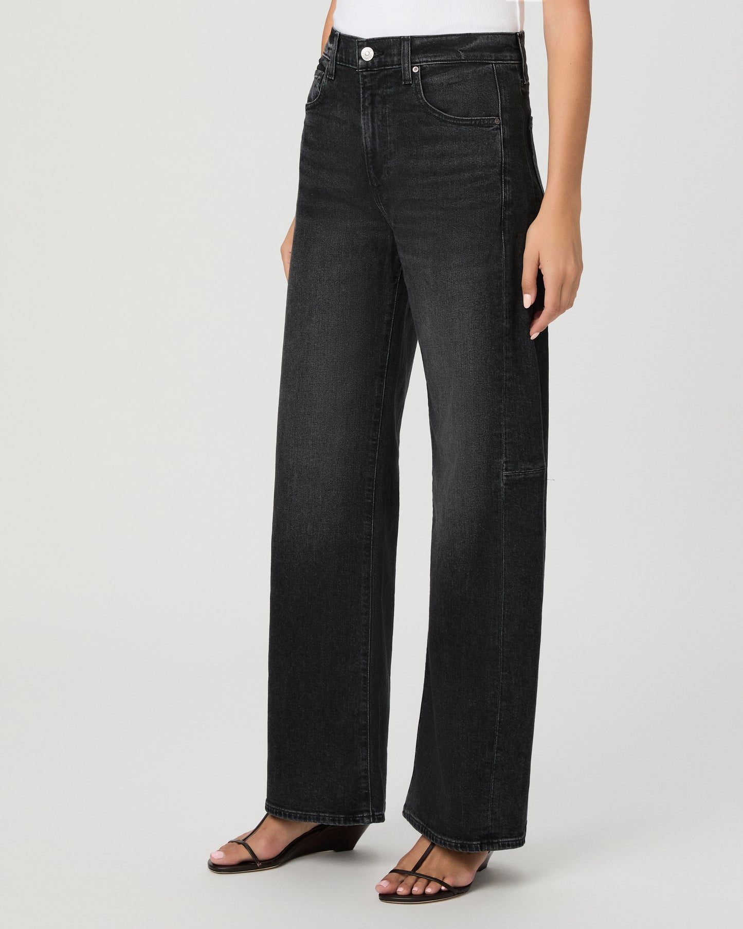 Woman wearing a white top paired with black  jeans and black sandals against a white background