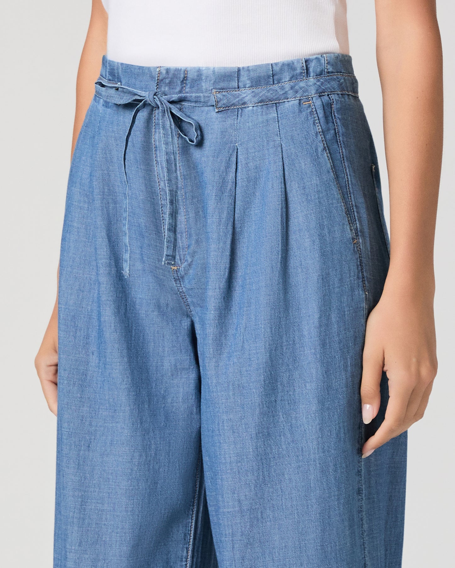 Woman wearing a blue sleeveless top and wide-leg jeans on a white background 