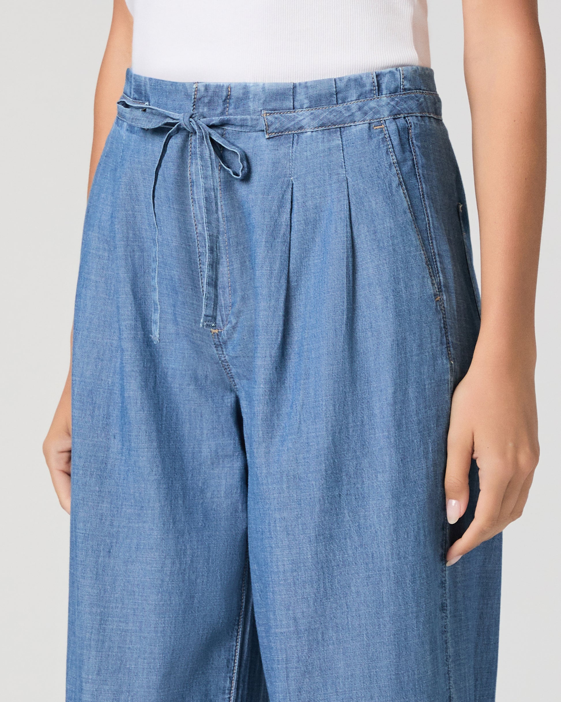 Woman wearing a blue sleeveless top and wide-leg jeans on a white background 