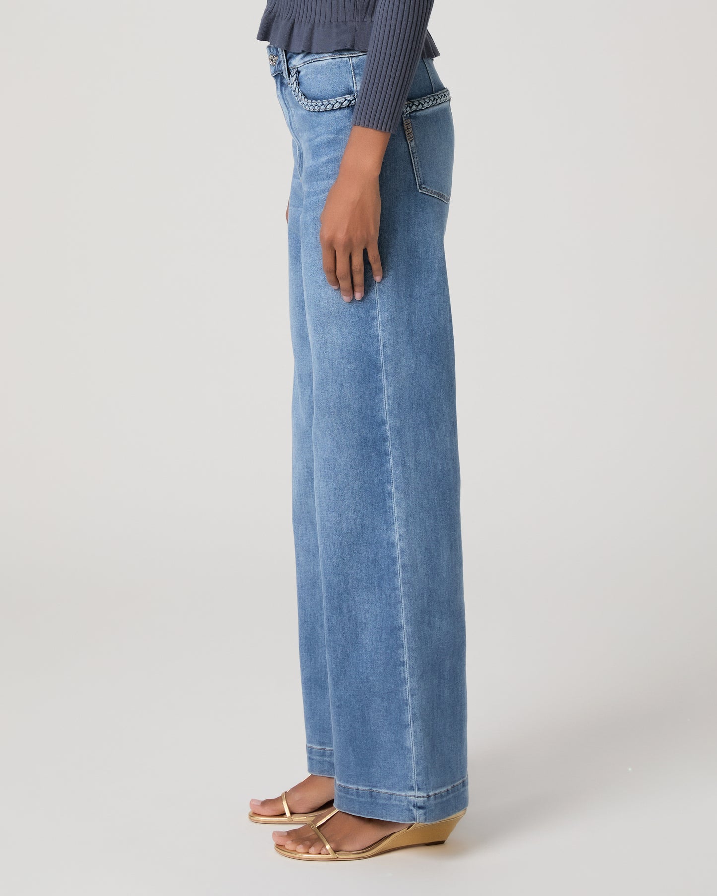 Woman wearing a blue long sleeve top and blue jeans and gold sandals on a white background
