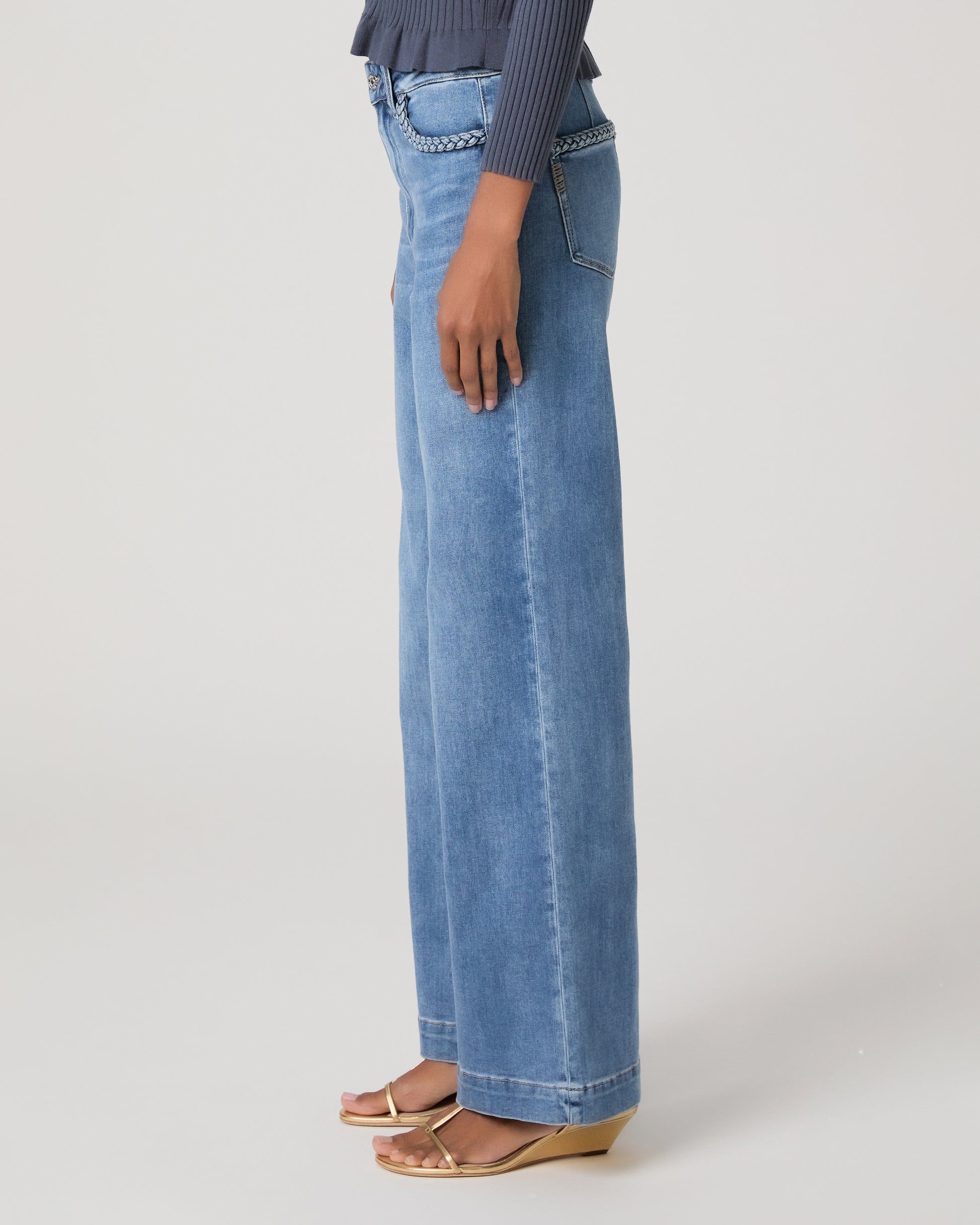 Woman wearing a blue long sleeve top and blue jeans and gold sandals on a white background