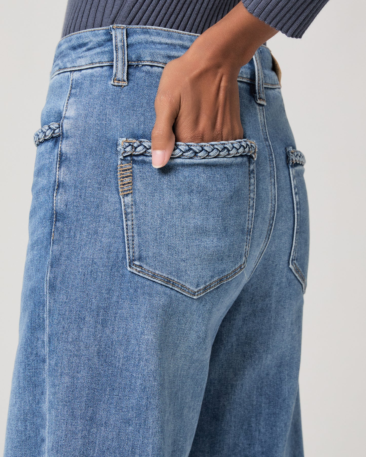 Woman wearing a blue long sleeve top and blue jeans and gold sandals on a white background