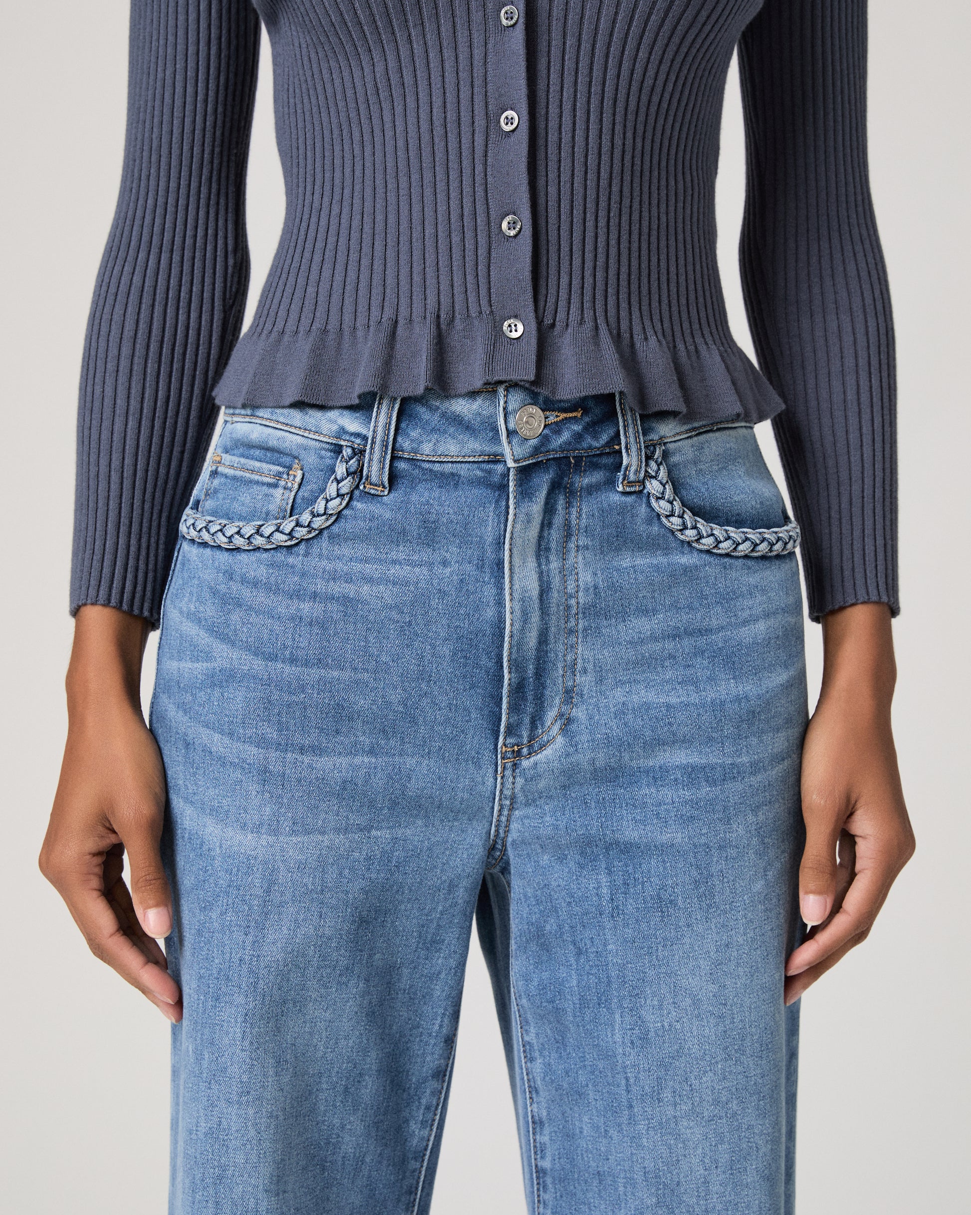 Woman wearing a blue long sleeve top and blue jeans and gold sandals on a white background