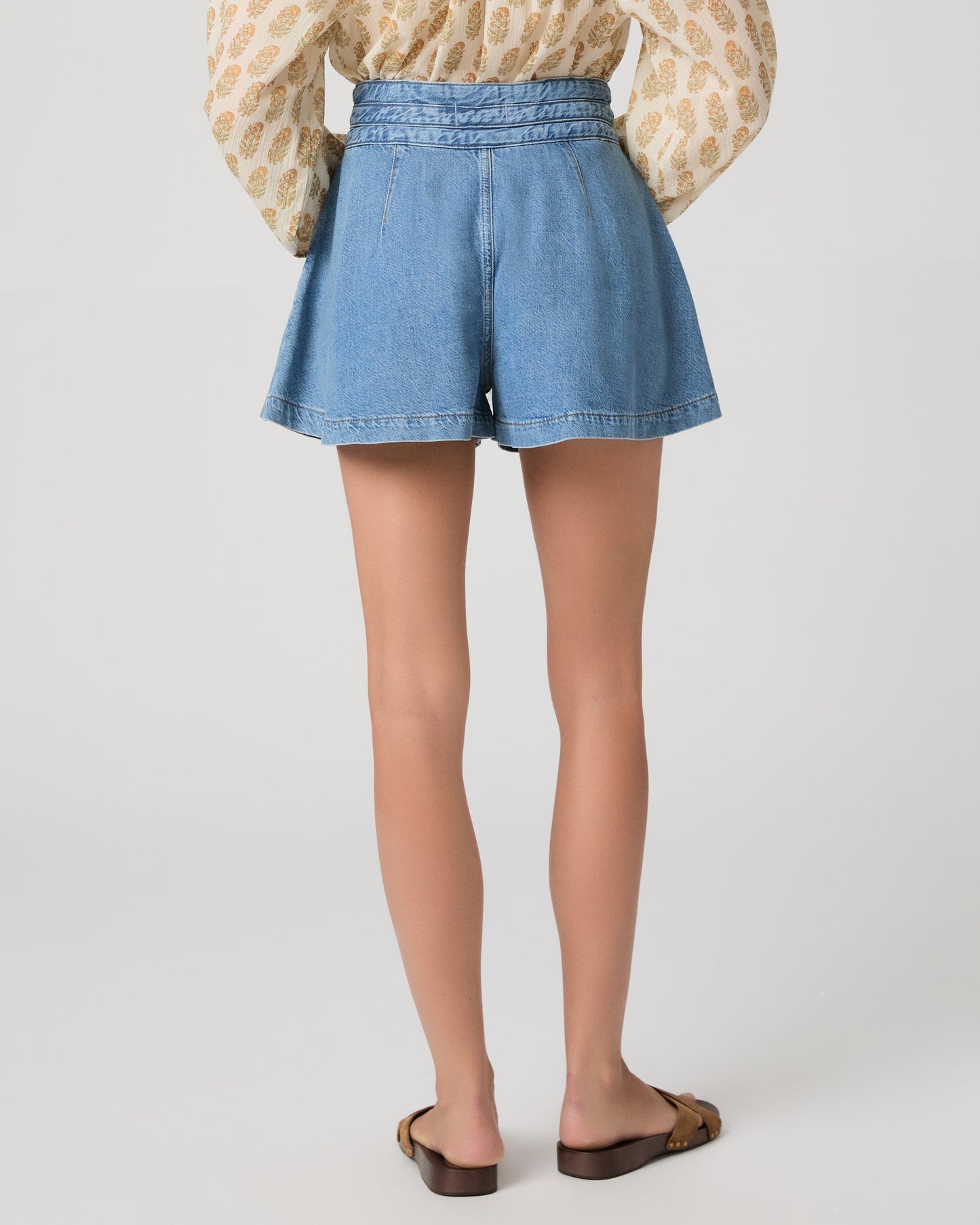Woman wearing a patterned blouse and denim shorts on a white background